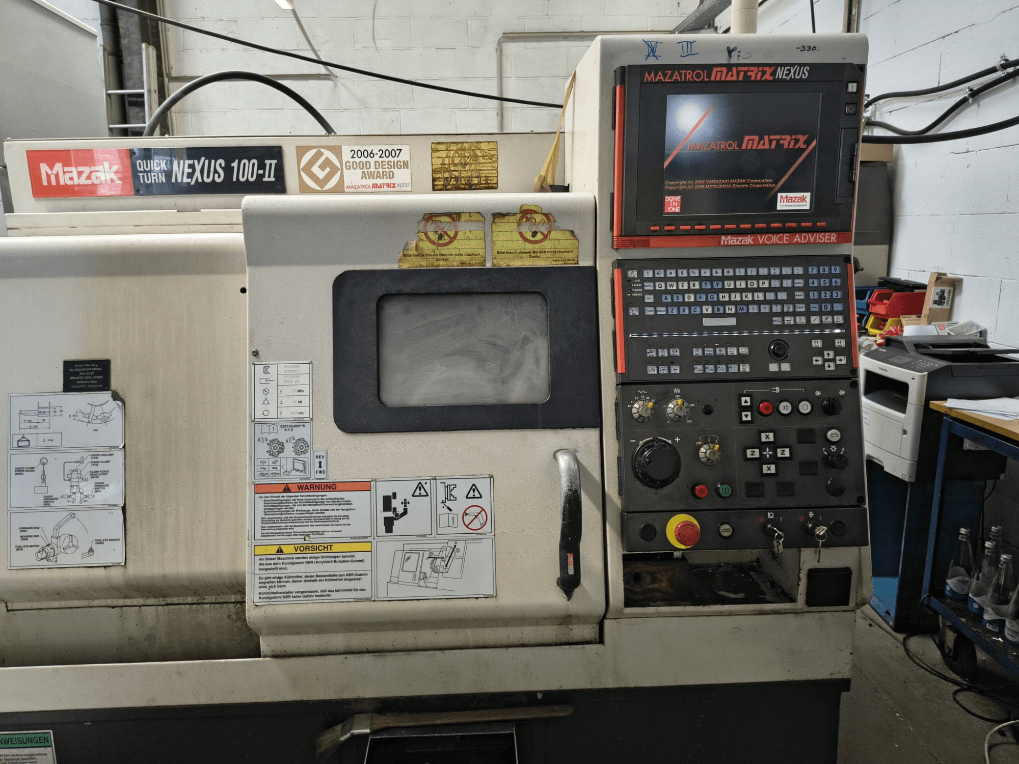 A Mazak Quick Turn Nexus 100-II vízszintes eszterga elölnézete, a vezérlőpanellel és a műszaki adatokat megjelenítő kijelzővel.