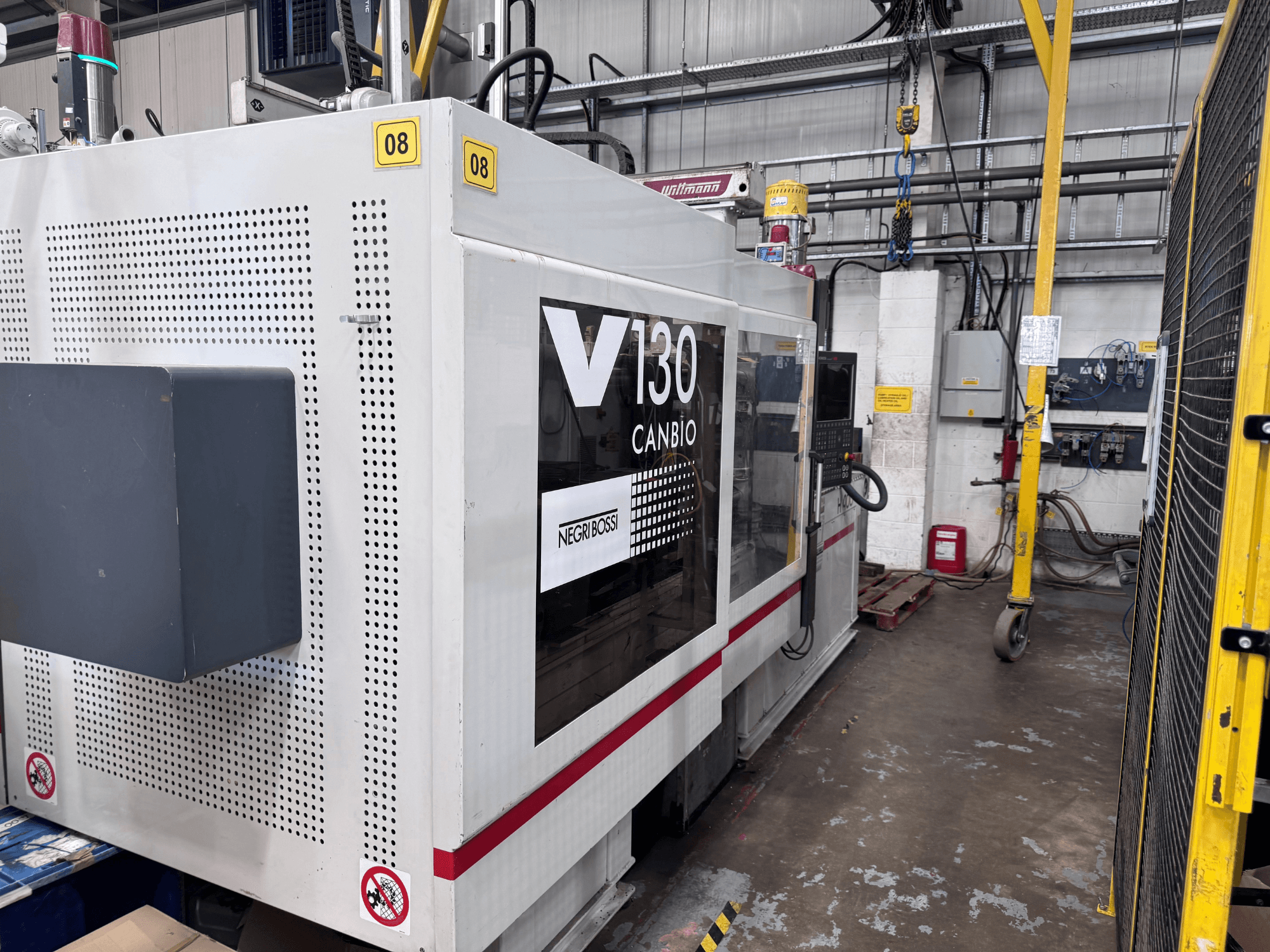 Negri Bossi 1300H-400 hidraulikus fröccsöntőgép, oldalnézet, a vezérlőpanellel és a biztonsági jelzésekkel együtt.