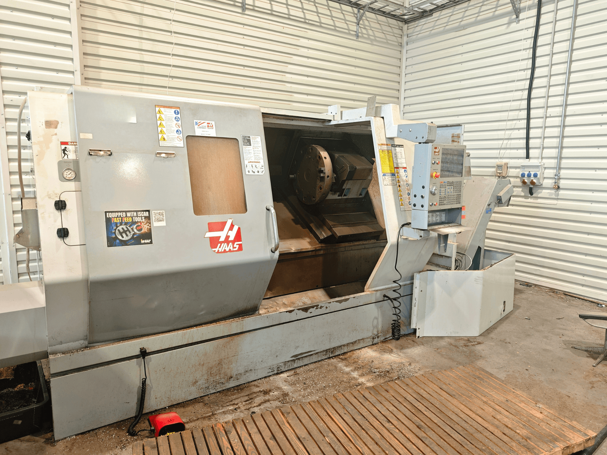 Haas SL-40HE vízszintes eszterga, elölnézet, amelyen látható a vezérlőpanel, a munkaterület és a biztonsági címkék.