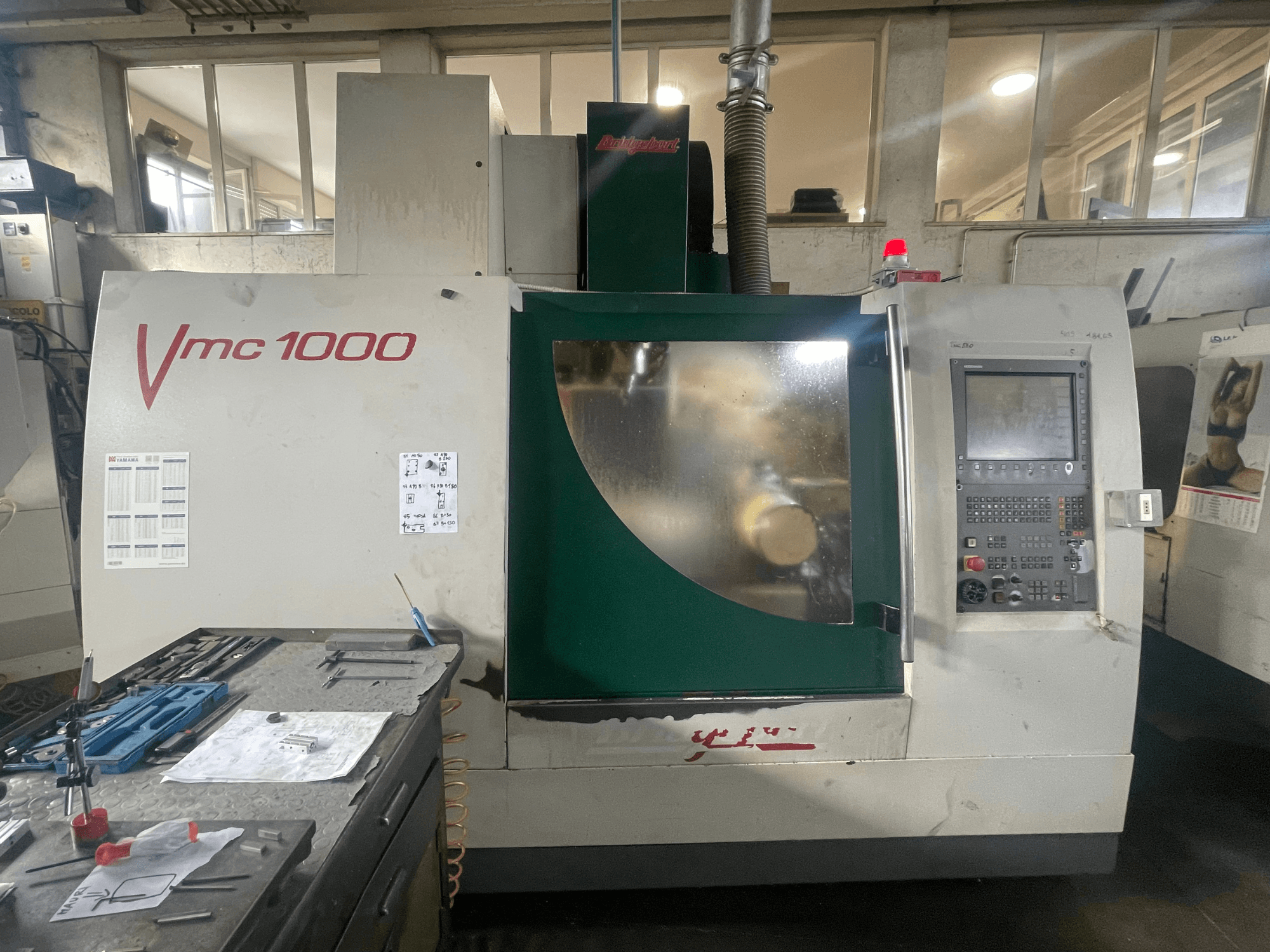 Bridgeport VMC 1000/30 függőleges megmunkáló központ, elölnézet, a vezérlőpanellel és a főtesttel, a közelben lévő szerszámokkal.