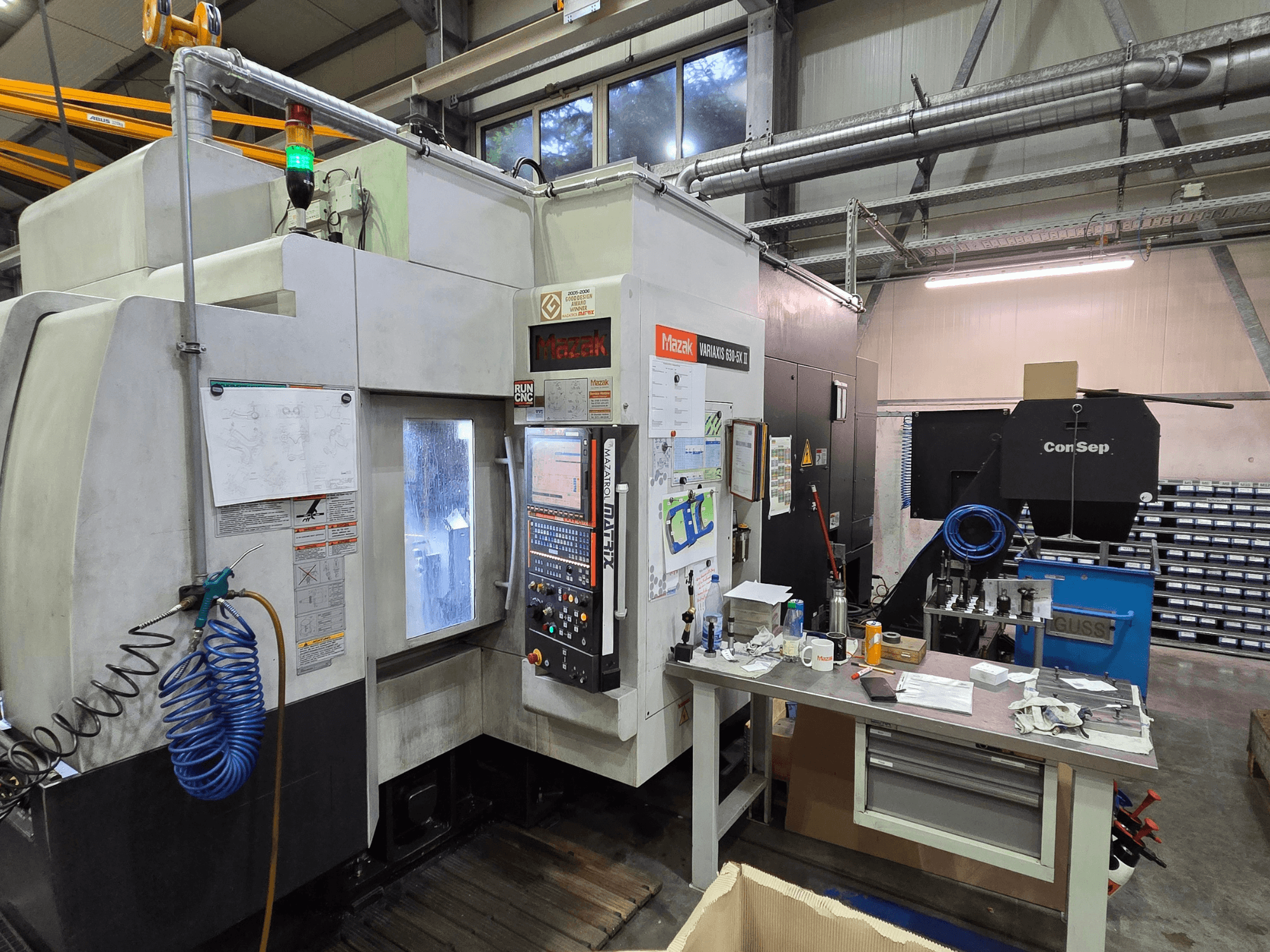 Mazak Variaxis 630-5X CNC-gép egy műhelyben, elölnézetben, vezérlőpanel, tömlő és tartozékok az oldalsó asztalon.