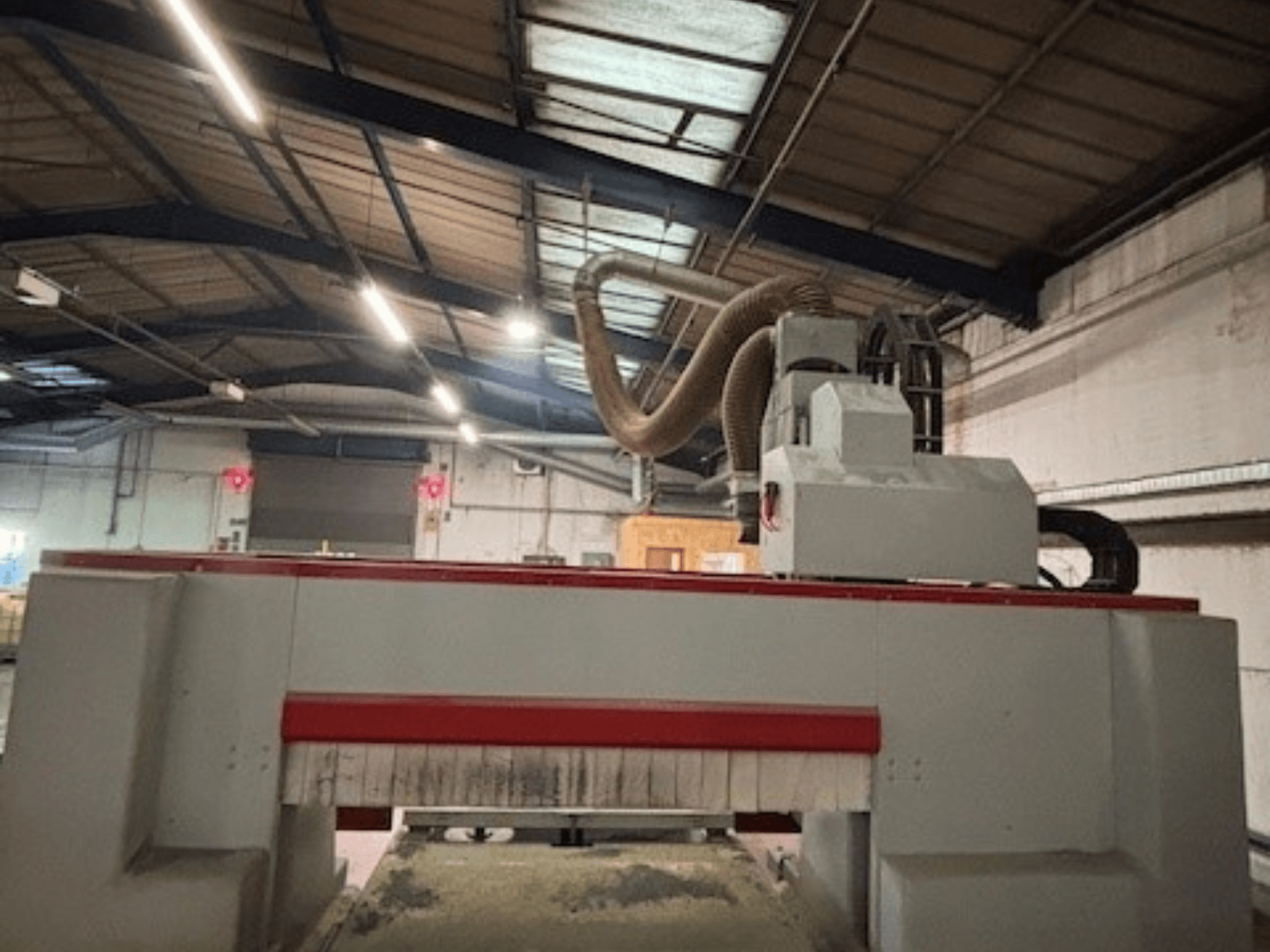 CNC-végmarógép egy műhelyben, oldalnézet, kiemelve a piros és szürke kialakítást, porelszívó rendszer csatlakoztatva.