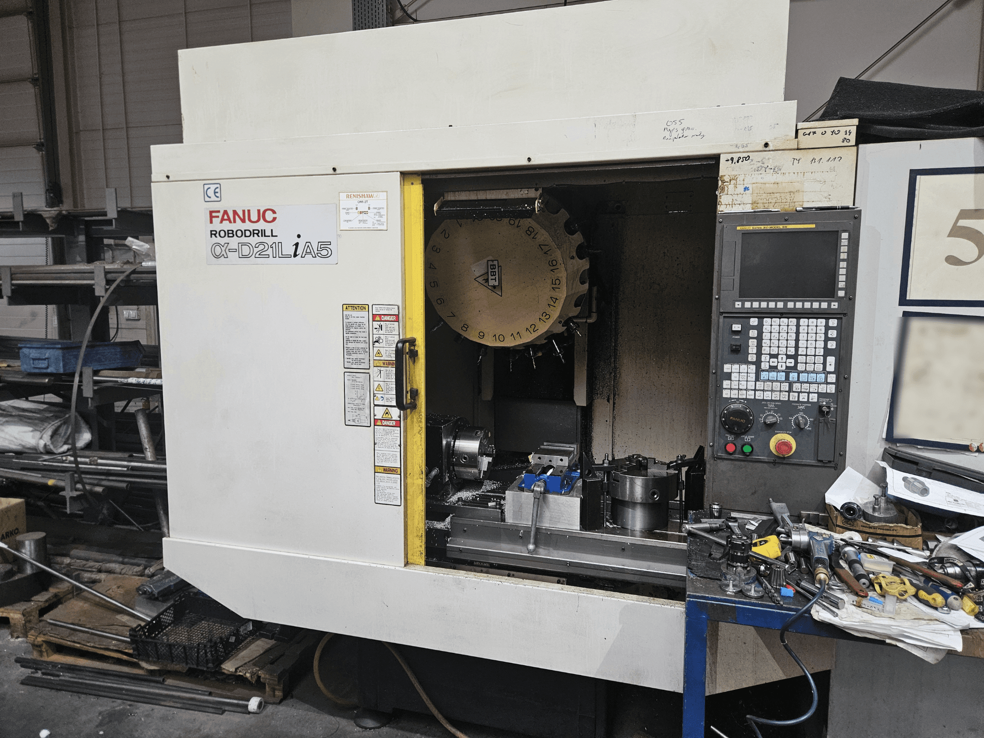 FANUC Robodrill α-D21LiA5, elölnézetben a szerszámtartó és a kezelőpanel, szerszámok és berendezések körül egy műhelyben.