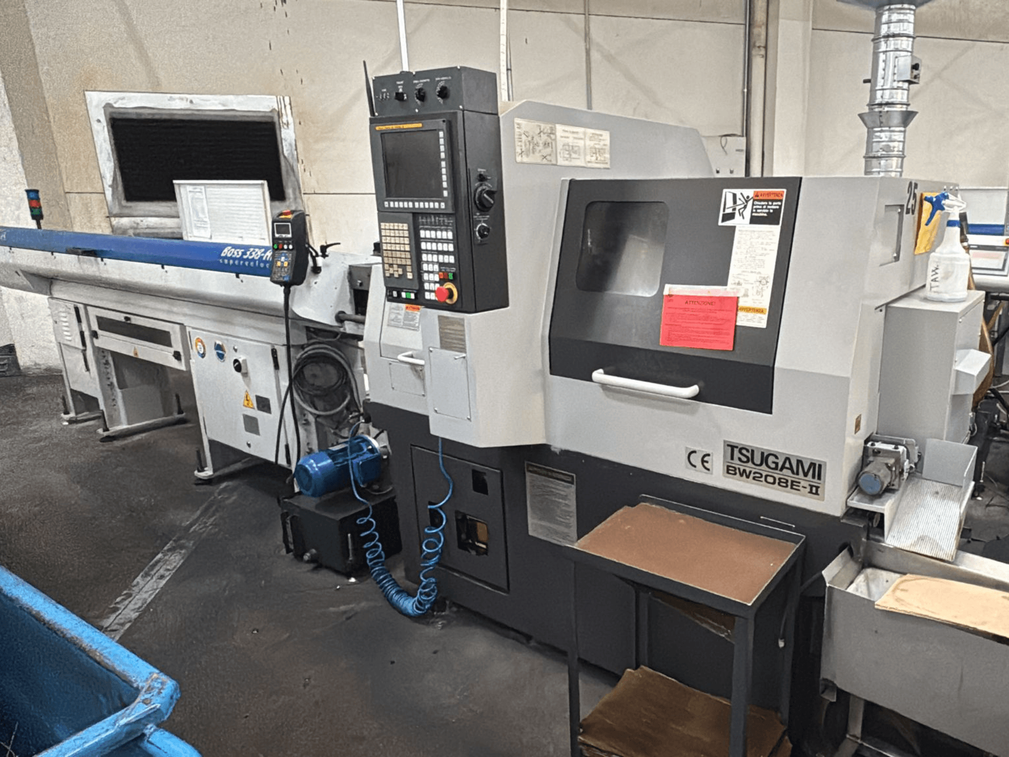 Tsugami BW208E-II CNC-gép egy műhelyben, szemből, a vezérlőpanel és a biztonsági címkék láthatóak.