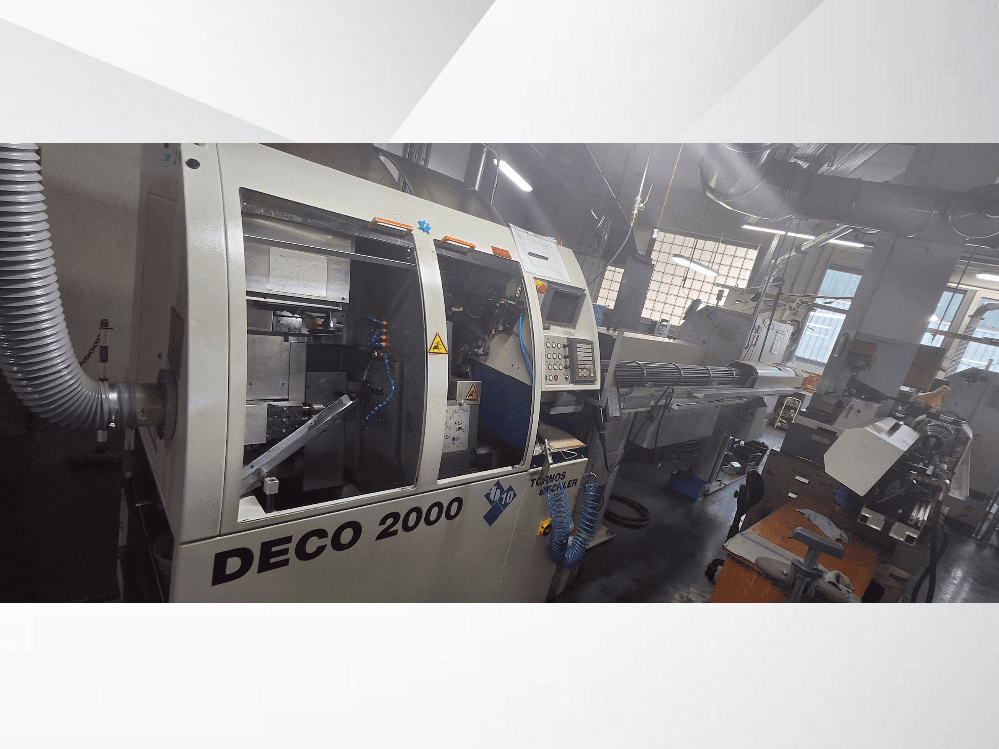 DECO 2000 CNC-gép egy műhelyben, elölnézetben, a kezelőszervek és egy hosszú munkadarab beállítása a jobb oldalon.