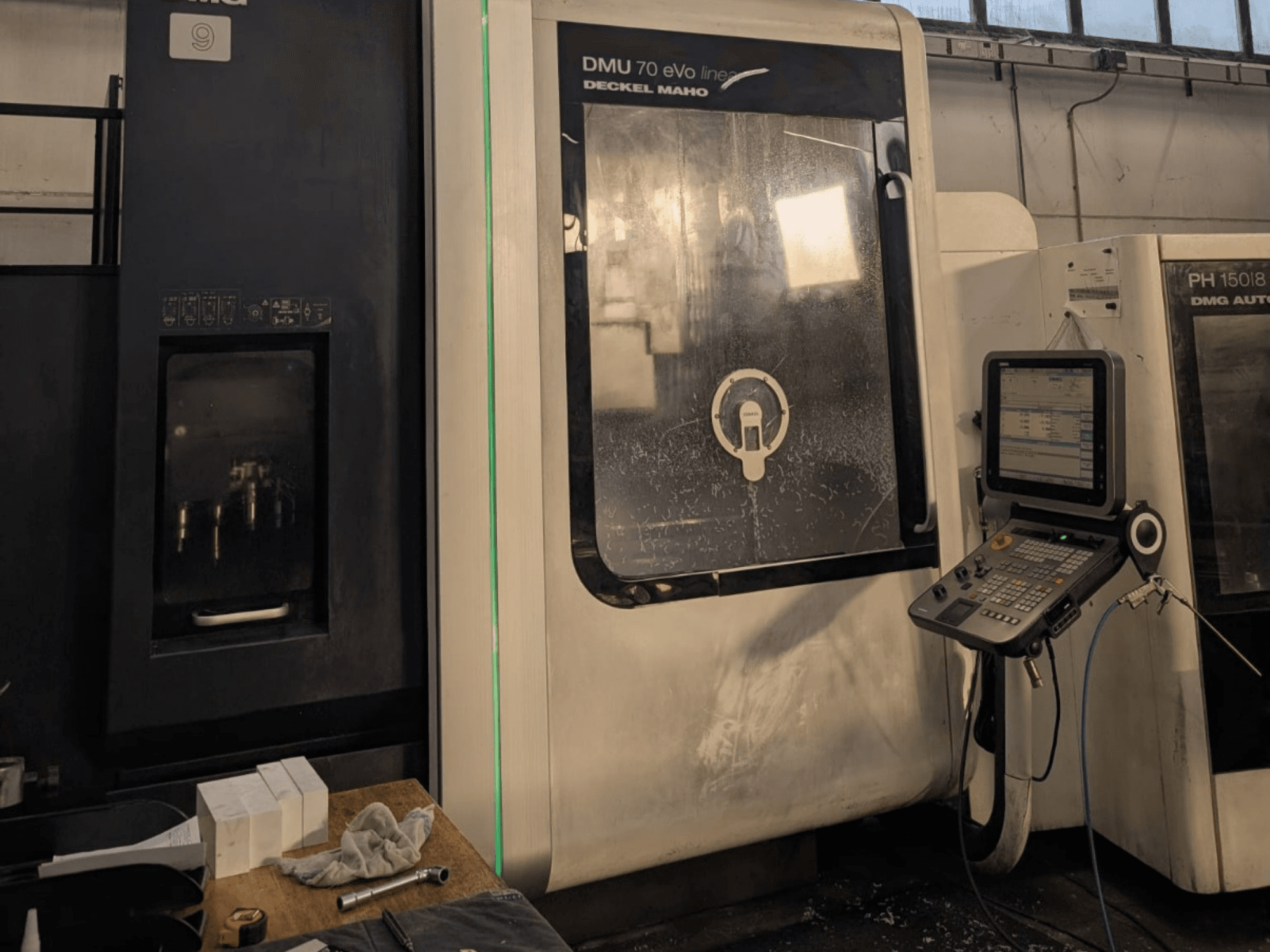 DMG DECKEL MAHO DMU 70 EVO Lineáris függőleges megmunkálóközpont, elölnézet a vezérlőpanel, a szerszámok és a munkaterület látható.
