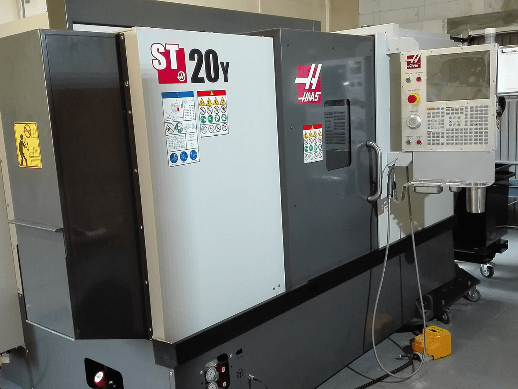 Haas ST20Y CNC esztergapad elölnézetben, a kezelőpanellel, a biztonsági címkékkel és a hűtőfolyadék-rendszerrel.