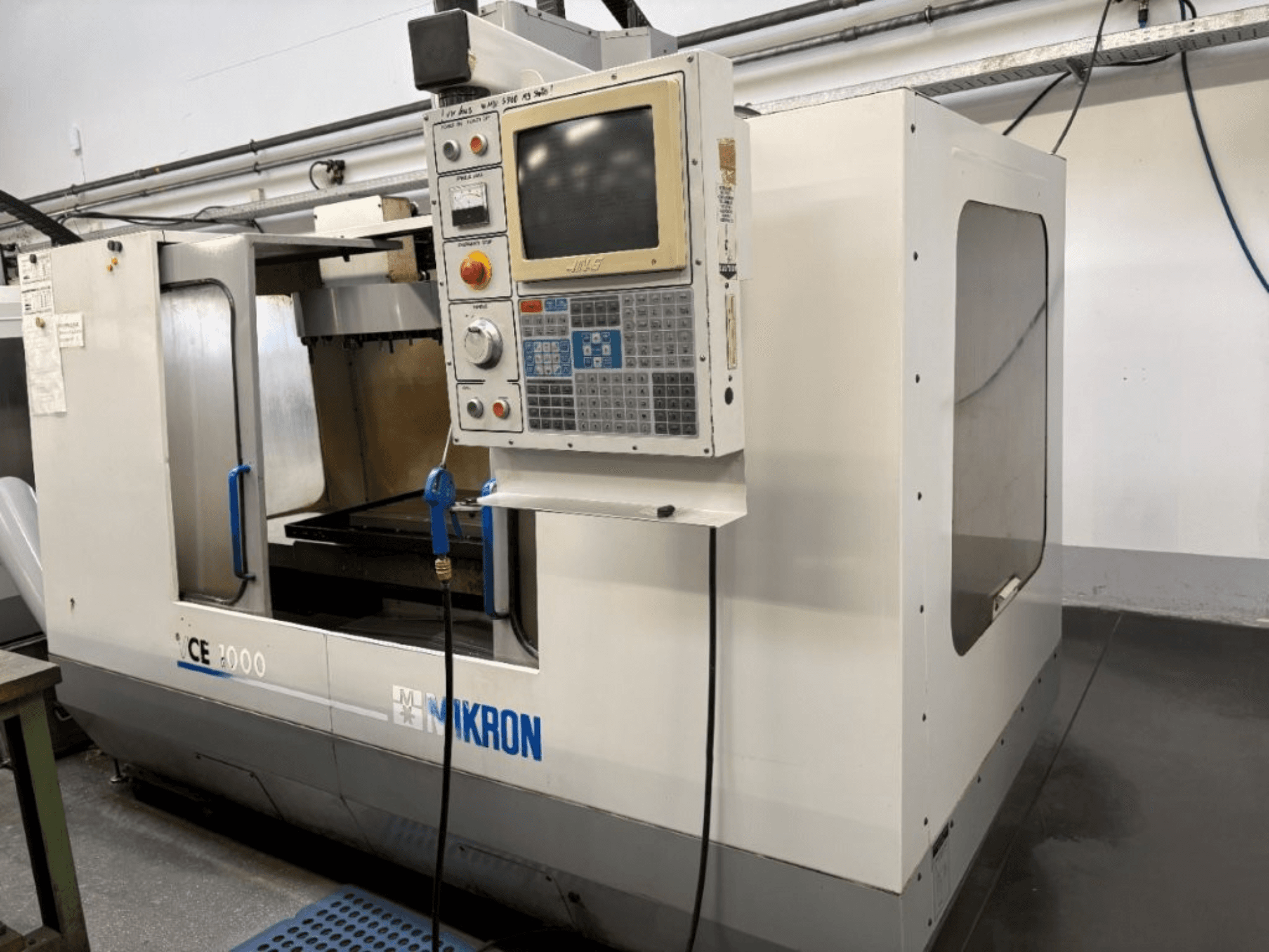 Mikron CE 2000 CNC gép, előlnézet; gombokkal és képernyővel ellátott vezérlőpanel, ezüst külső és munkaterület.
