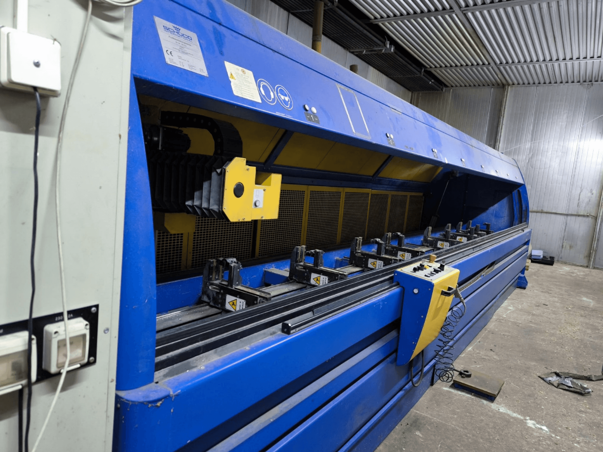 Schneider ipari vágógép kék színben, oldalnézetben, látható a vezérlőpanel, a szalagok és a több szorítóállomás.
