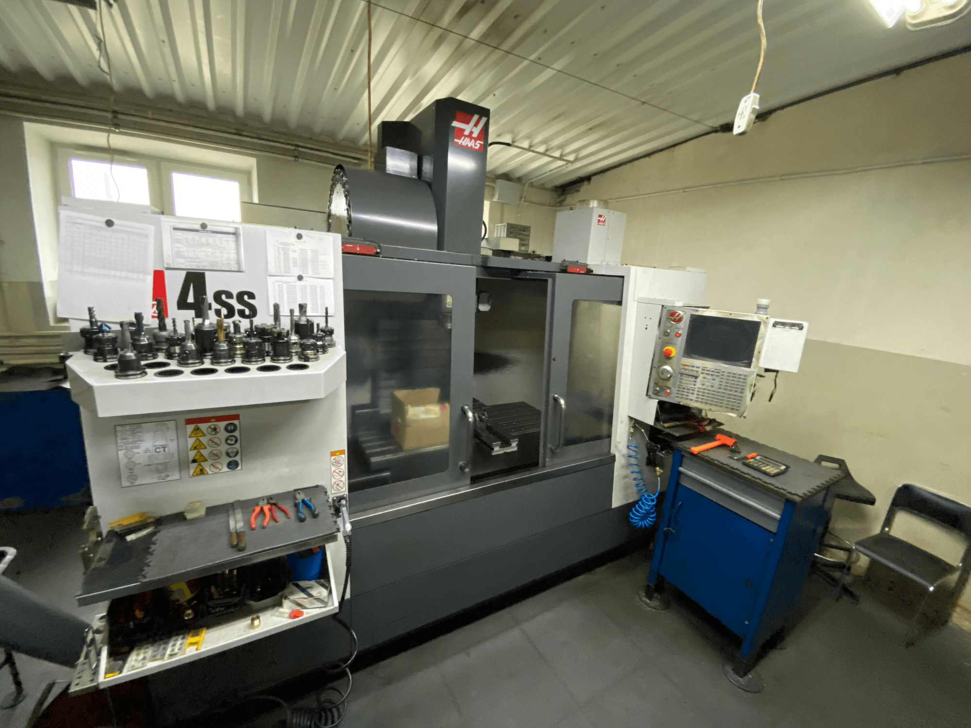 Haas VF-4SS függőleges megmunkáló központ, elölnézet szerszámtartókkal és vezérlőpanellel. A felszerelt szerszámok és a munkaterület jól láthatóak.