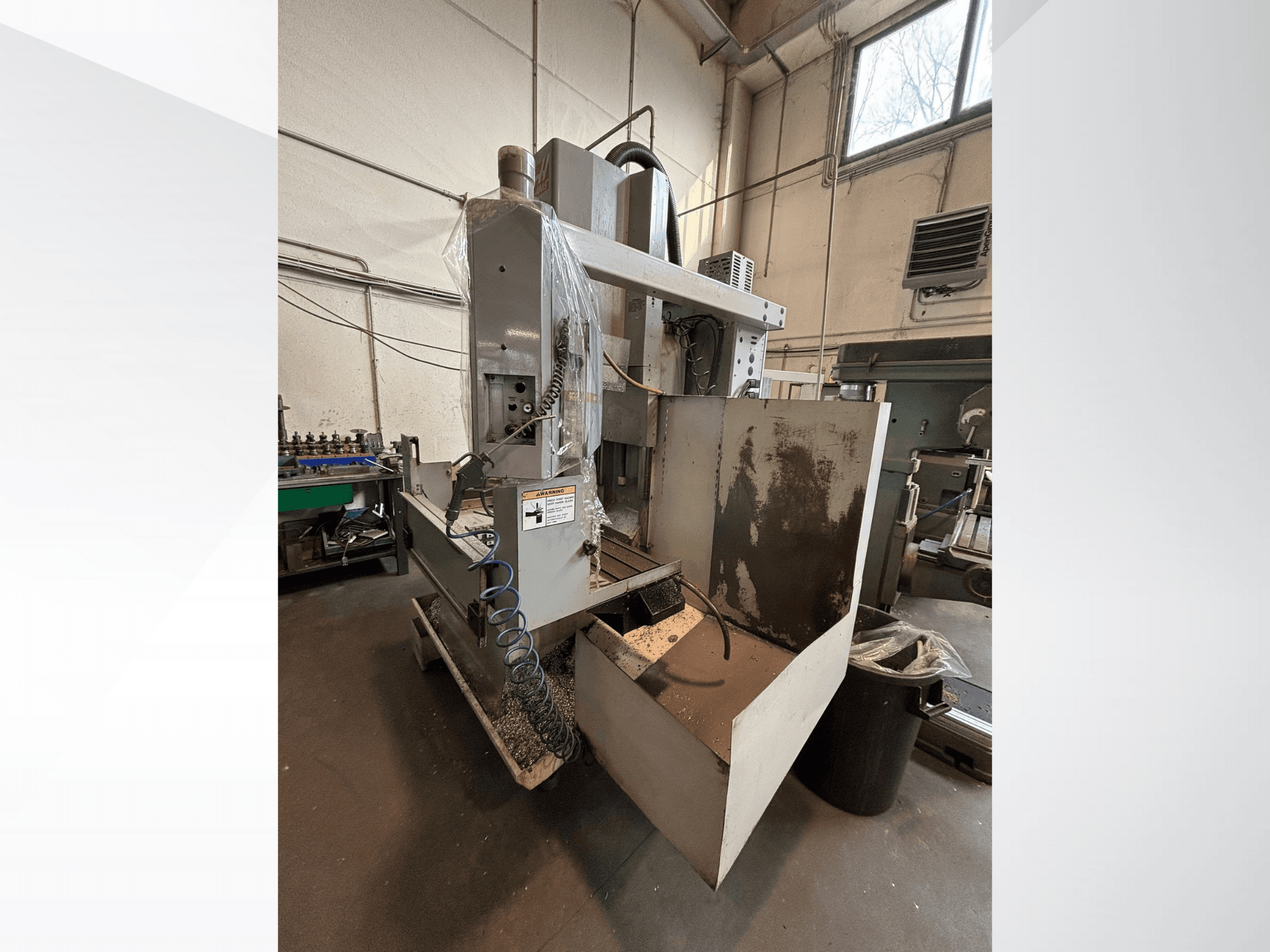 Függőleges marógép védőburkolattal, oldalnézet; a hűtőfolyadék-tömlő és a vezérlőpanel látható. Ideális megmunkáláshoz.