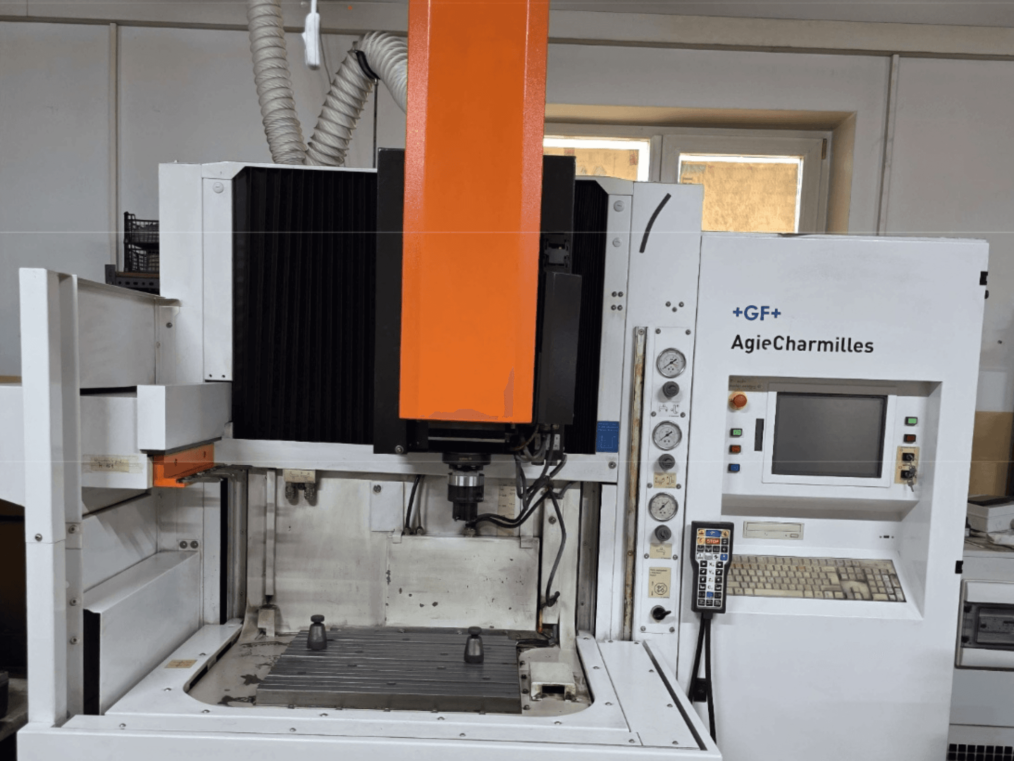 AgieCharmilles megmunkálóközpont elölnézetben, nagy narancssárga orsóval, vezérlőpanellel és látható munkaasztallal.