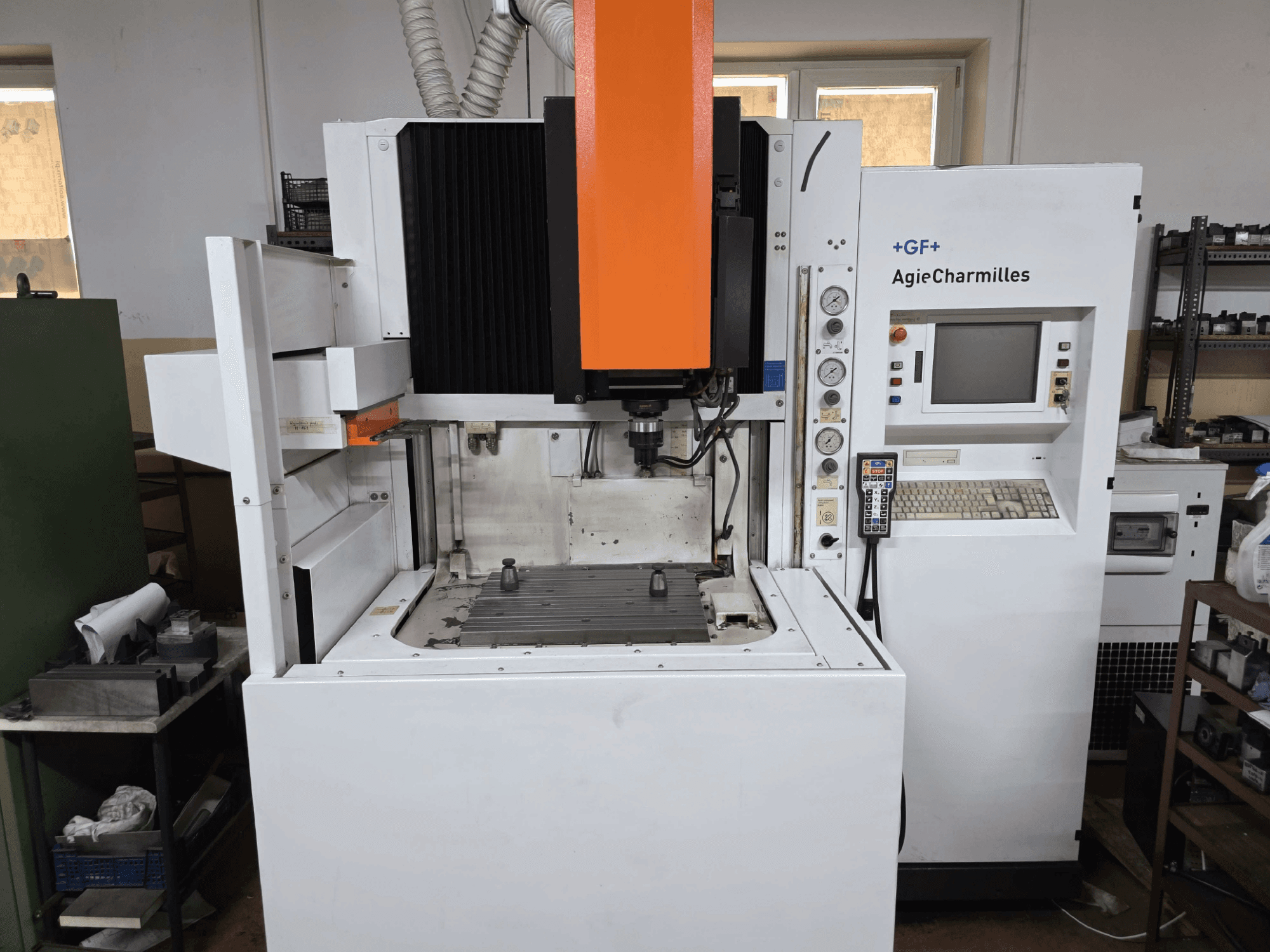 GF AgieCharmilles CNC-gép, elölnézetben, kiemelkedő narancssárga orsóval, digitális vezérlőpanellel és szerelt fúróasztallal.