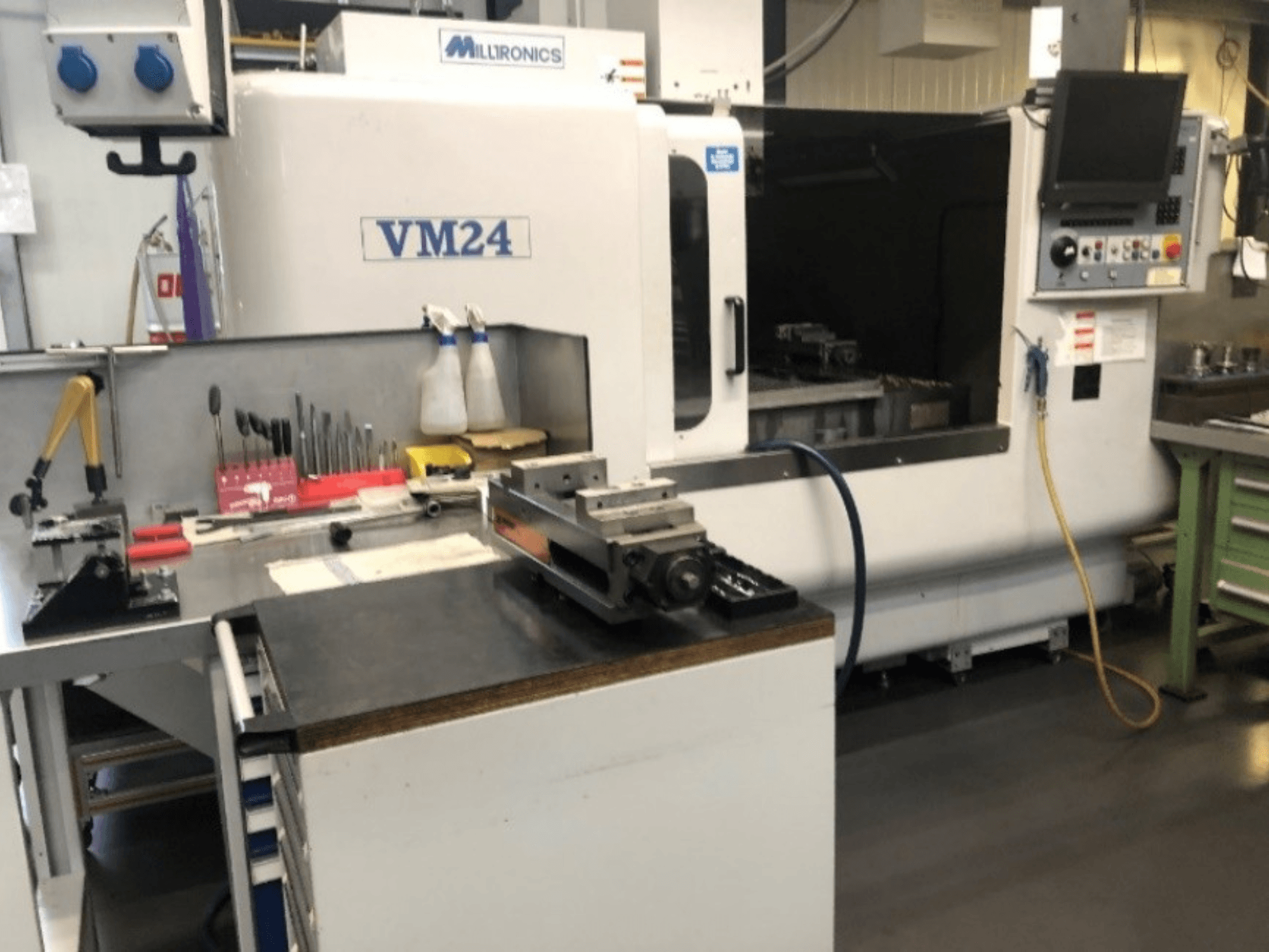 A Milltronics VM24 CNC-gépet tartalmazó gépi munkaterület. Előlnézet a szerszámokkal és berendezésekkel egy munkapadon.
