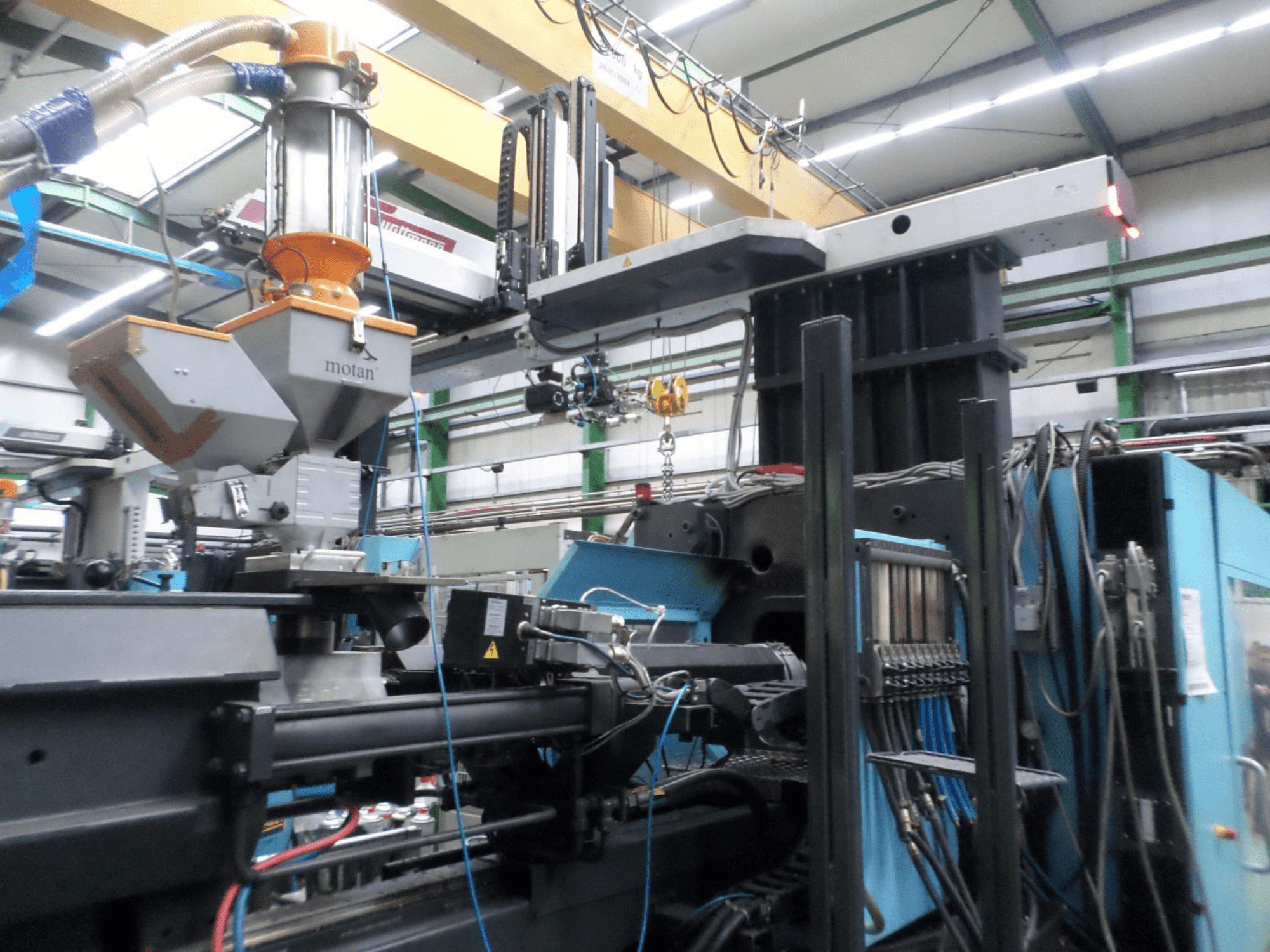 DEMAG D 1300 hidraulikus fröccsöntőgép, oldalnézet, amelyen látható a betöltőtartály, a vezérlőegység és a csatlakozások gyári beállításban.
