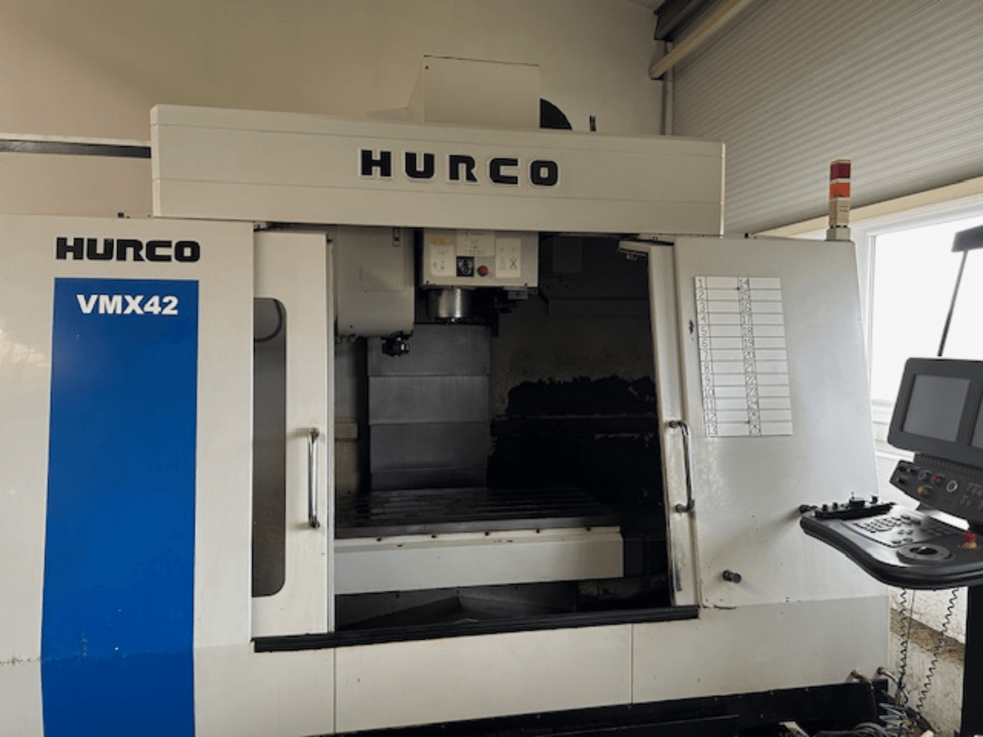 Hurco VMX42 CNC-gép elölnézetben, a vezérlőpanel, az orsó és a munkaterület látható; feltárja a működési elrendezést.