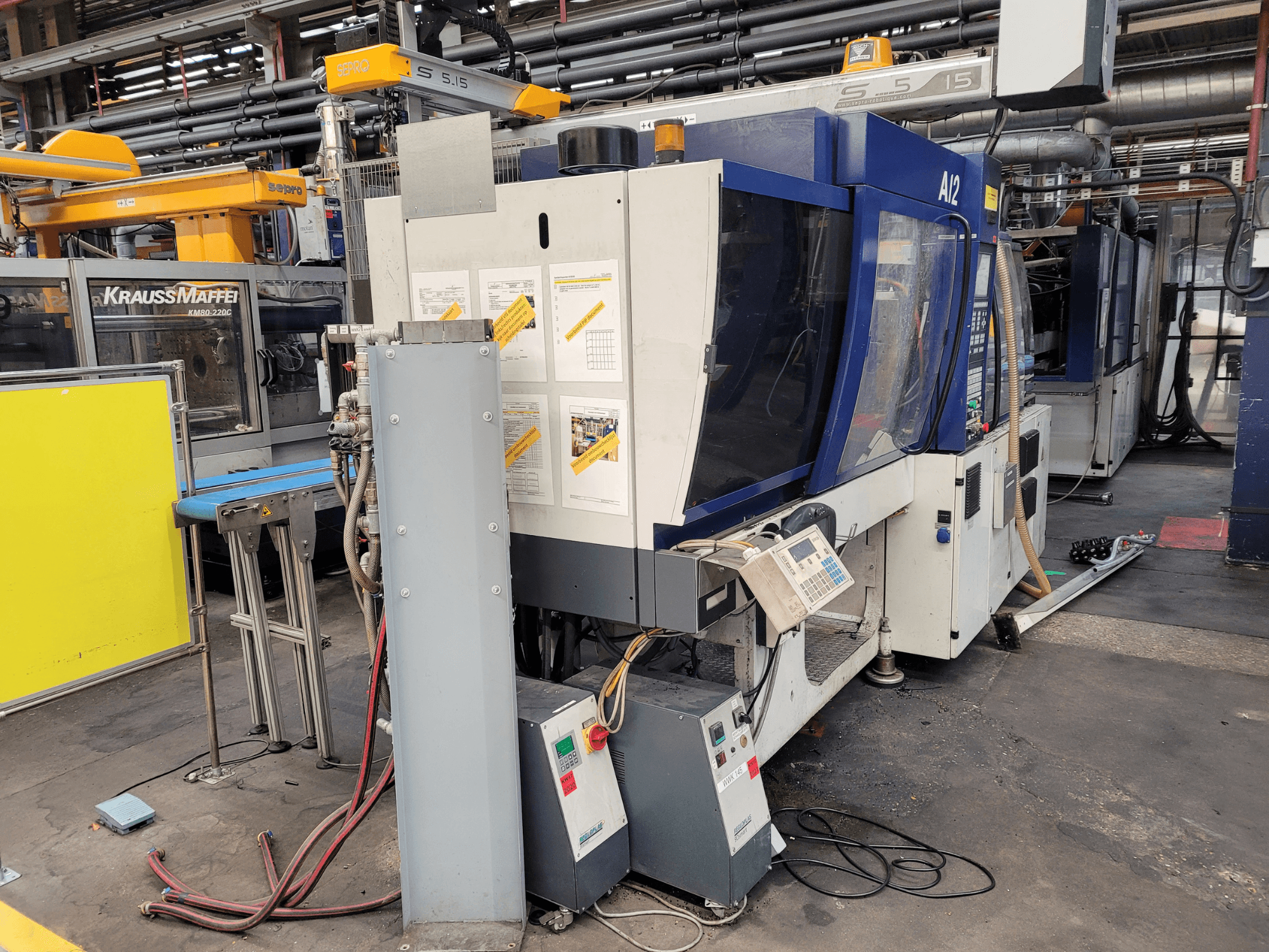 KraussMaffei KM80-232G típusú fröccsöntőgép, előlnézet, a vezérlőpanel és a működési alkatrészek.