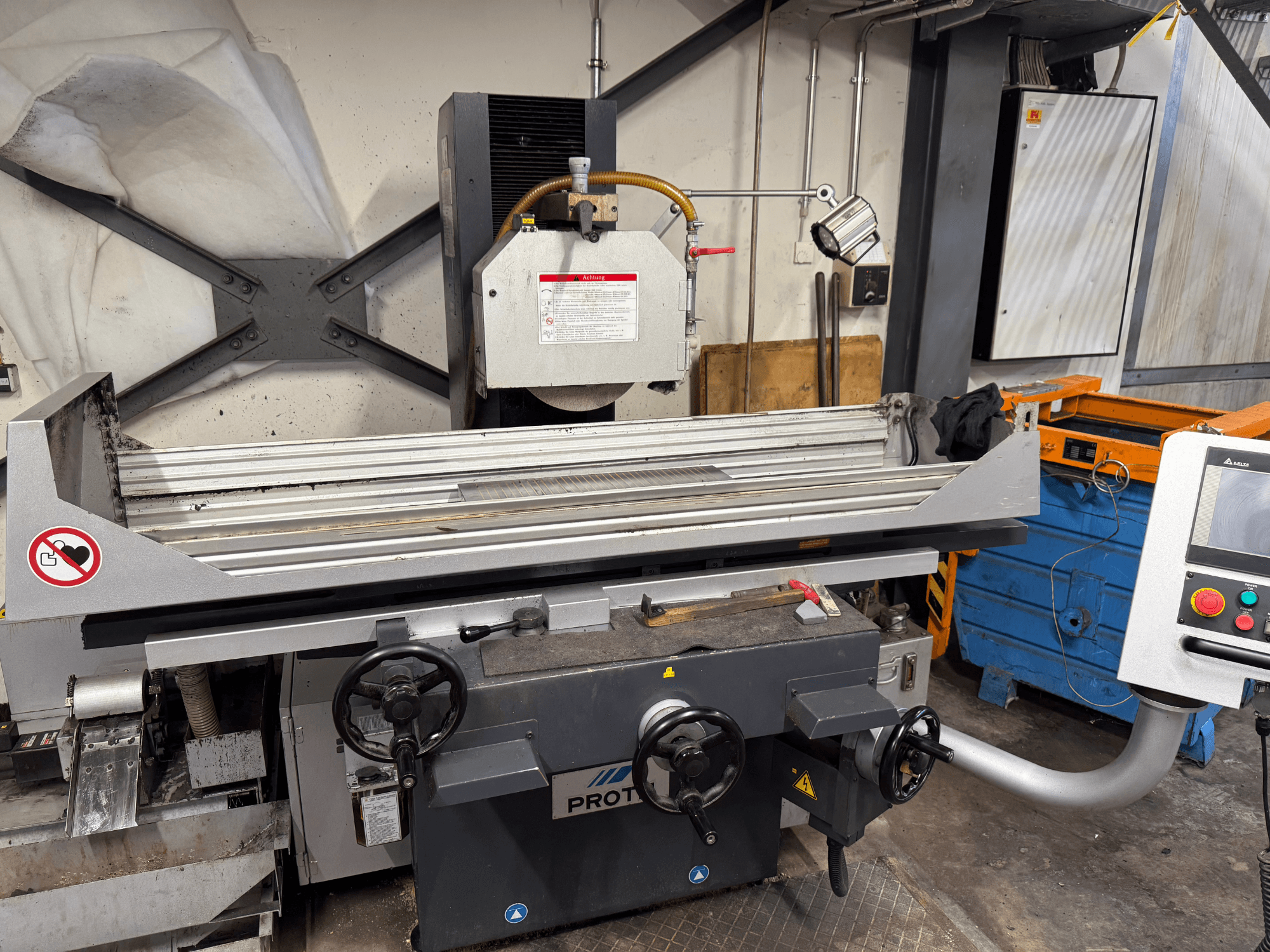 PROTEC gép, előlnézet, amely egy kézi vezérléssel, biztonsági figyelmeztetésekkel és hűtőrendszerrel ellátott felületcsiszolót mutat.