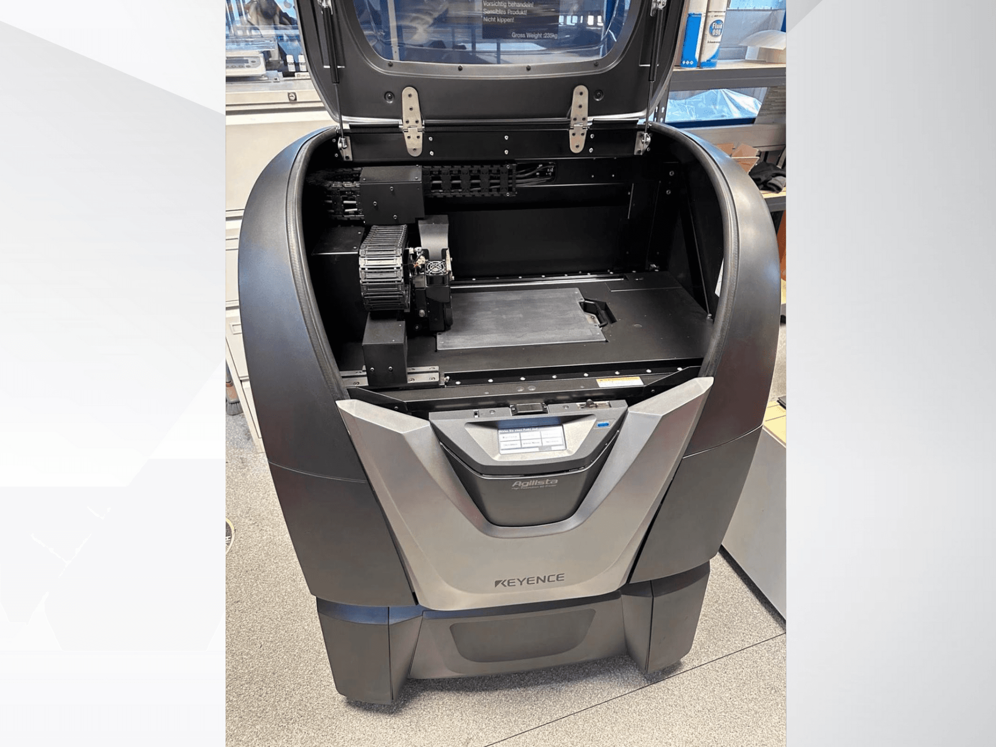 KEYENCE Agilista 3D nyomtató, előlnézet, a nyitott teteje, a nagy építési platform és a belső mechanikus alkatrészek.