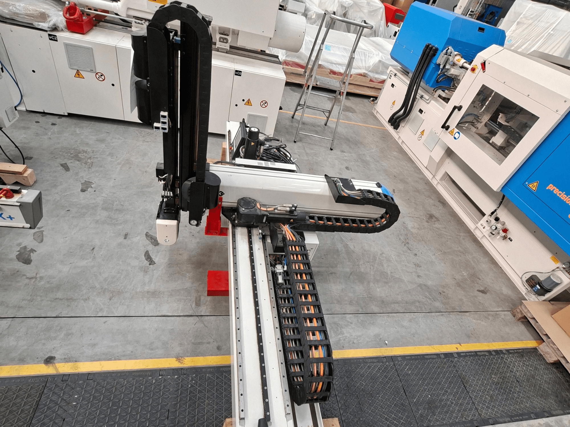 A Krauss Maffei LRX150-MC5 műanyag-feldolgozó gép felülnézetben, a gyárpadlón látható robotkarral és kábelcsatornával.