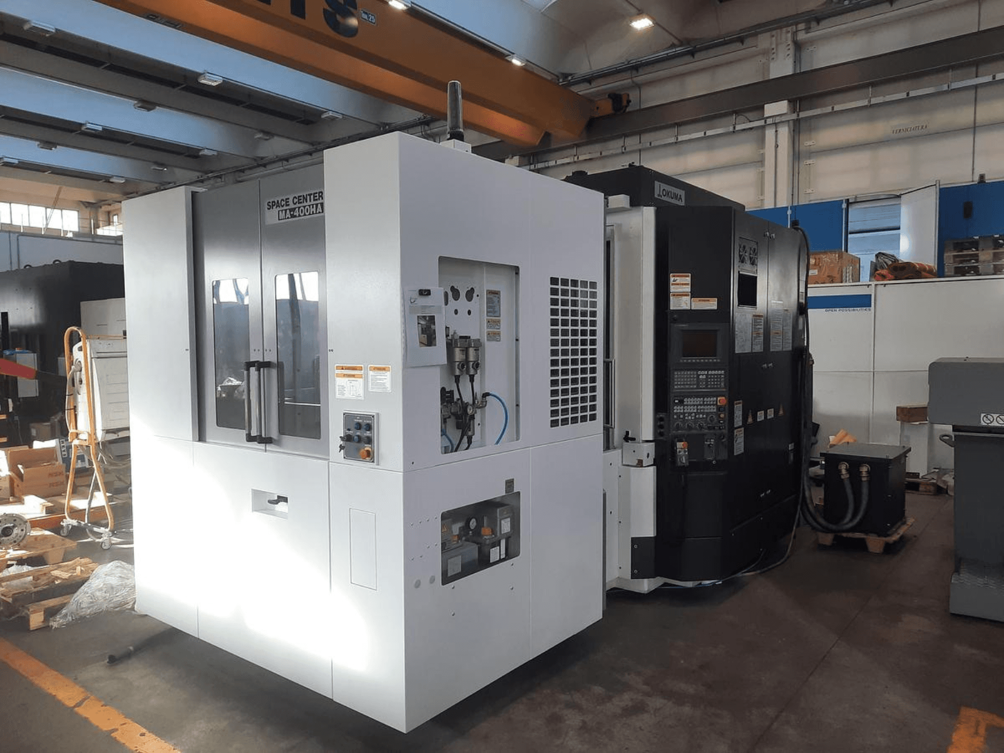 A SPACE CENTER IM-400HAA és OKUMA CNC gépek előlapja, a különböző vezérlők és a gyártó feliratai.