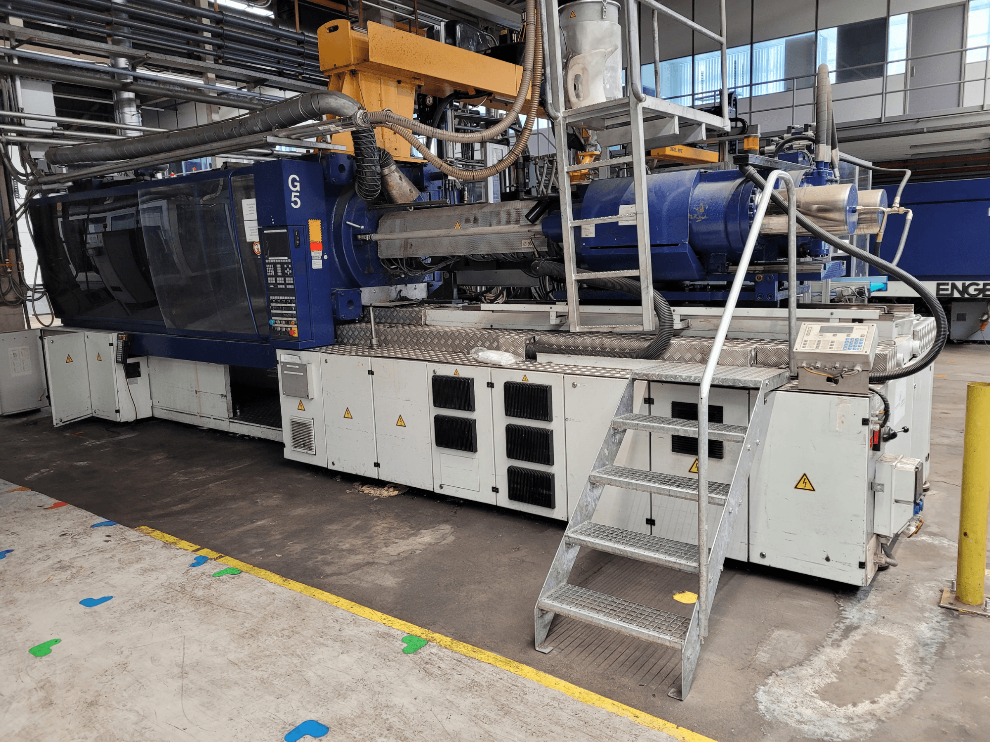 G5 fröccsöntőgép, oldalnézet, látható a vezérlőpanel, a lépcsős létra és a rozsdamentes acél munkafelület.