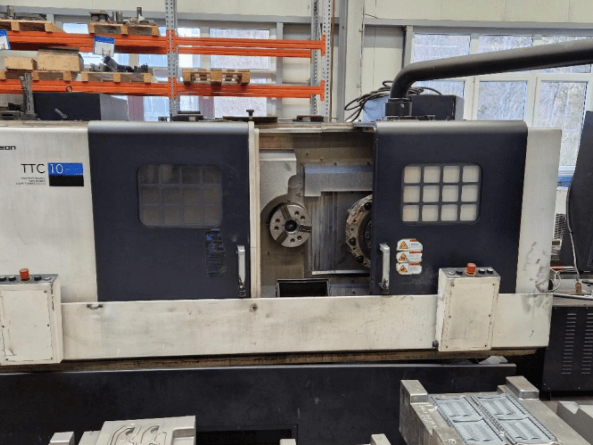 TTC 10 esztergagép előlnézetben, a vezérlőpanel, a látható tokmányok és a fém alkatrészeket tartalmazó munkaterület látható.