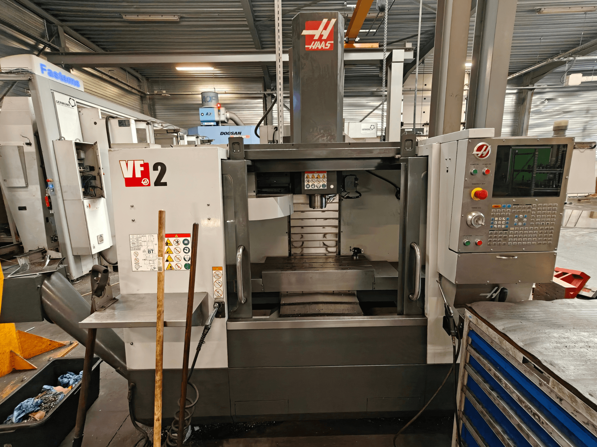 HAAS VF-2 függőleges megmunkáló központ, elölnézet, amelyen a kezelőszervek, az orsó és a munkapad láthatóak egy műhelyi környezetben.