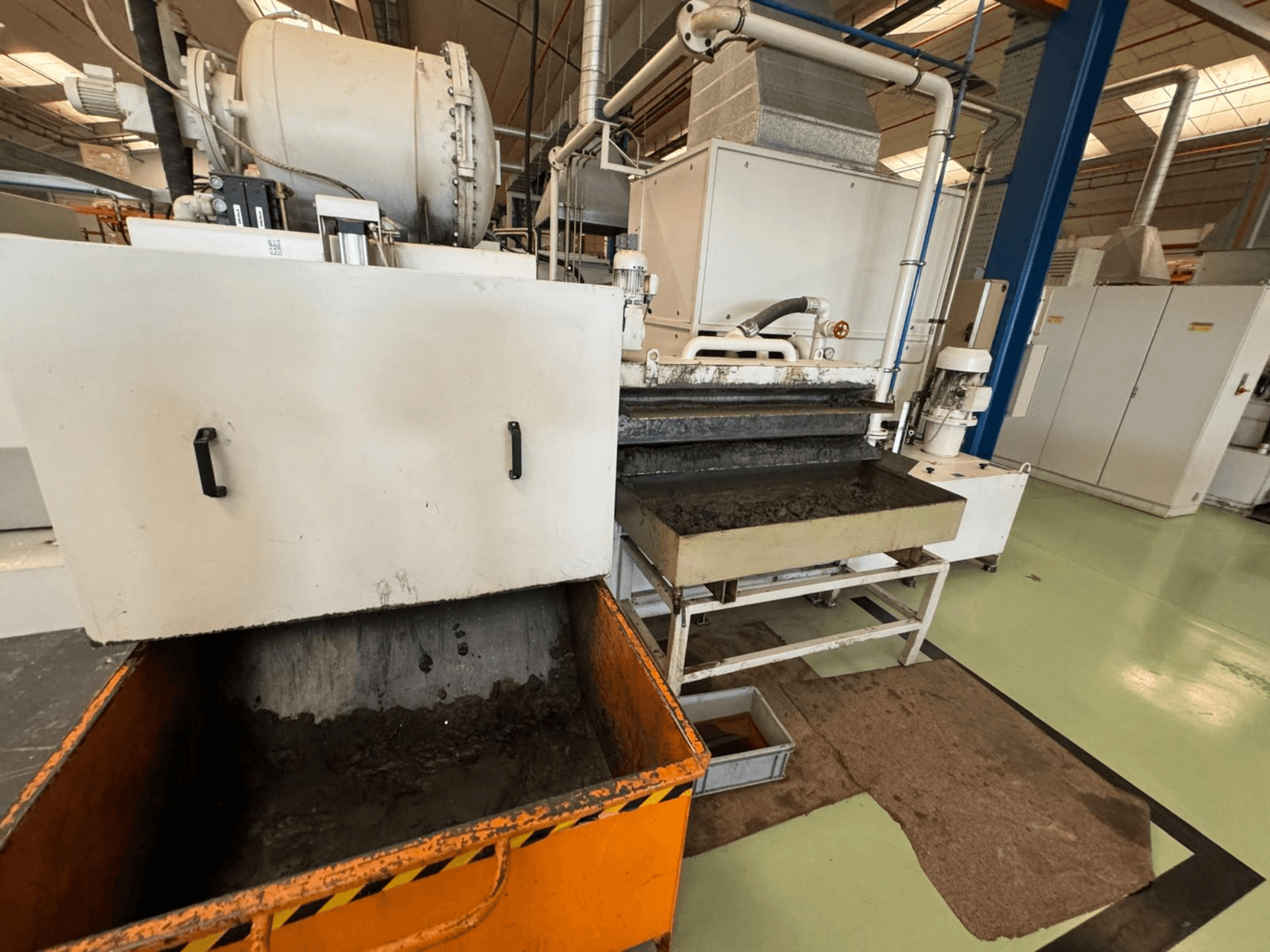 Ipari feldolgozó berendezés narancssárga hulladékgyűjtővel, elölnézetben; tartalmaz egy motort, szállítószalagokat és karbantartási területet.