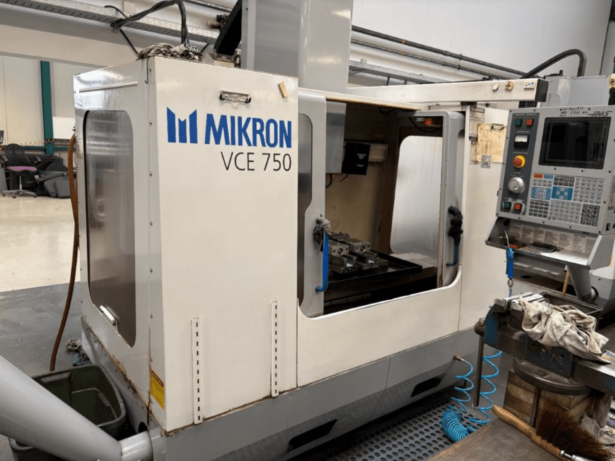 Mikron VCE 750 CNC marógép előlnézetben, megmunkált munkaasztallal és különböző gombokkal és képernyőkkel ellátott kezelőpanellel.