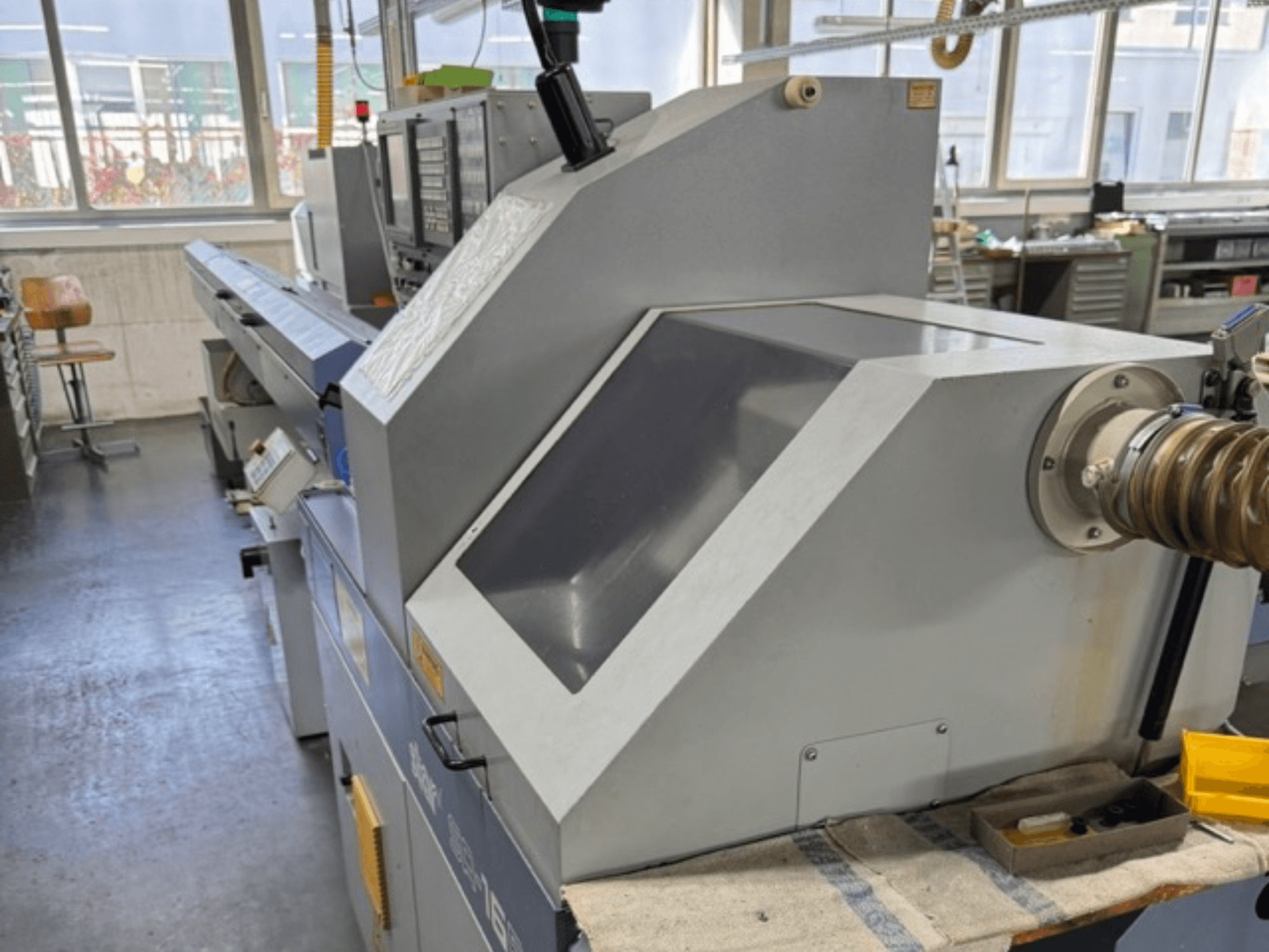 Szürke ipari gép oldalról nézve, nagy, szögletes panellel, vezérlőgombokkal és tömlőcsatlakozóval.