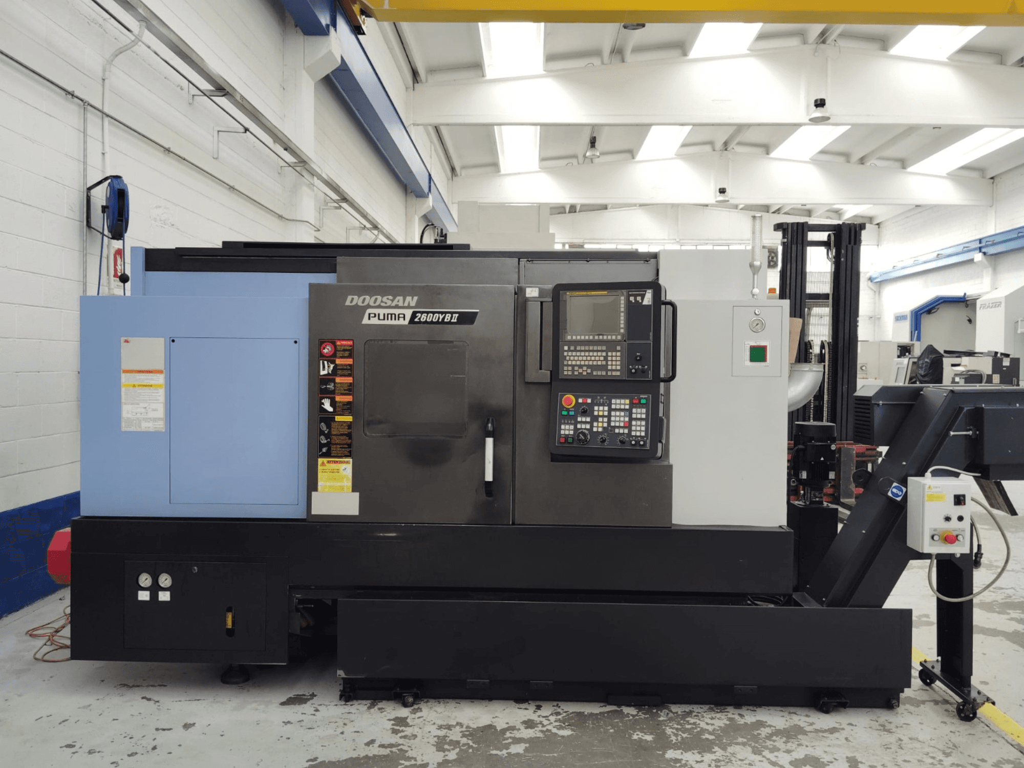 A DOOSAN Puma 2600YB II vízszintes esztergagép elülső nézete a kezelőpanellel és a biztonsági címkékkel.