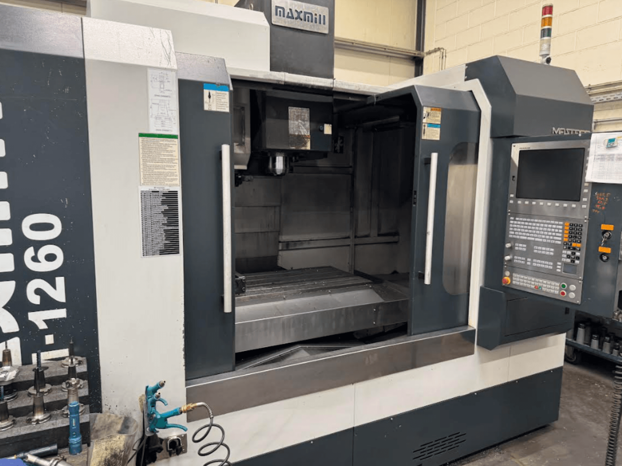 Maxmill CNC marógép, M-1260 modell, elölnézetben üres munkaterület a kezelőpanellel és a kezelési útmutatóval.