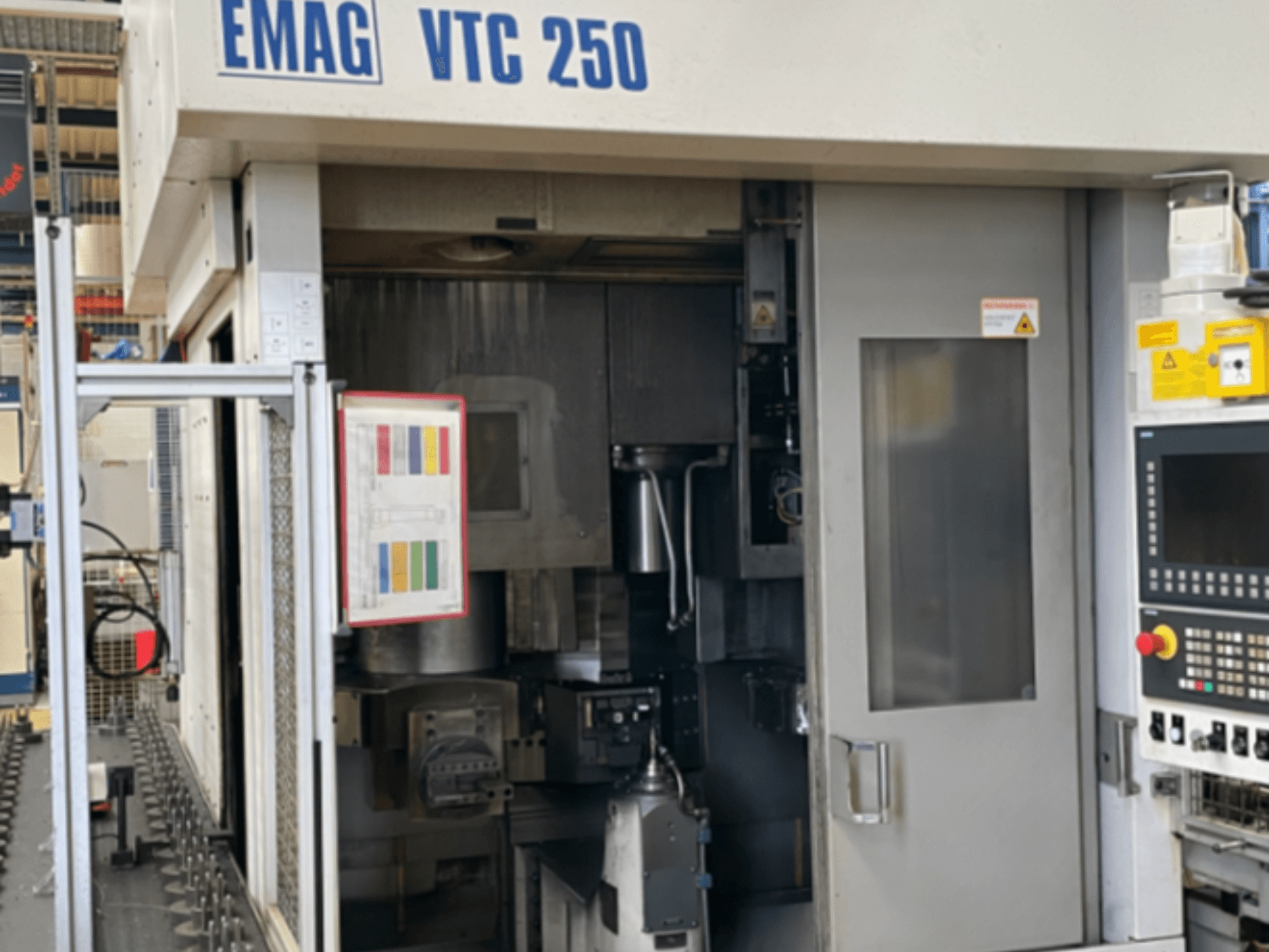 Az EMAG VTC 250 függőleges eszterga elölnézete, amelyen látható a vezérlőpanel, a kezelőfelület és a nyitott ajtó.