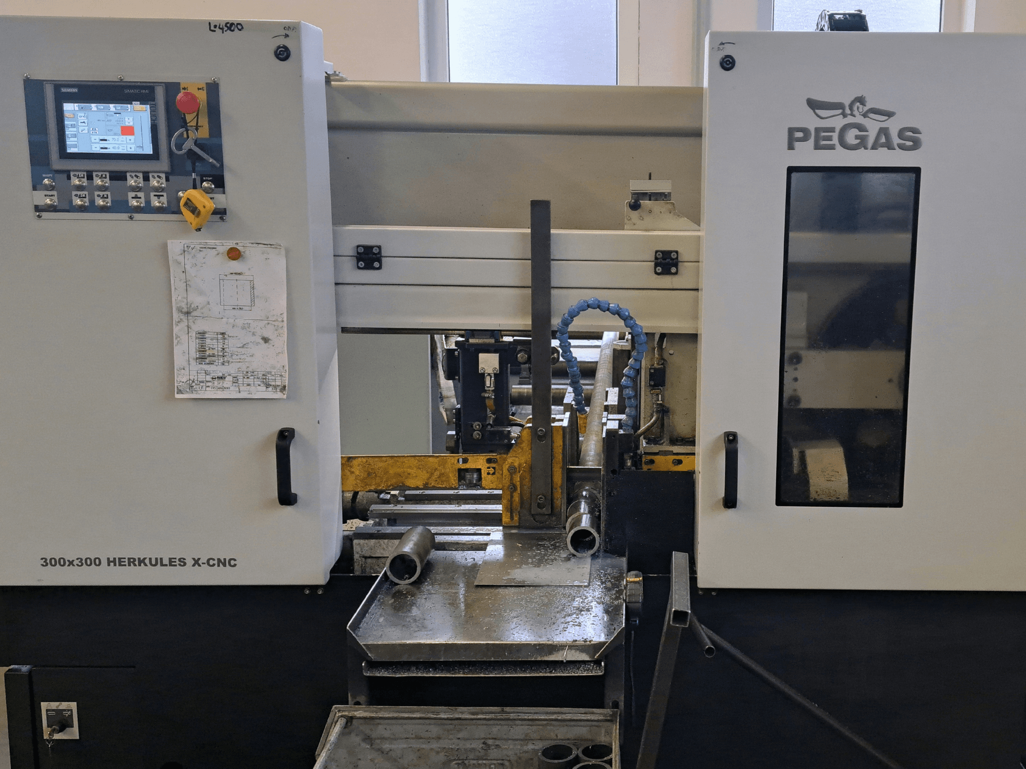 Pegas HERKULES X-CNC 300x300 lemezmegmunkáló gép, elölnézet, amelyen látható a vezérlőpanel és a fémdarabokkal ellátott munkaterület.