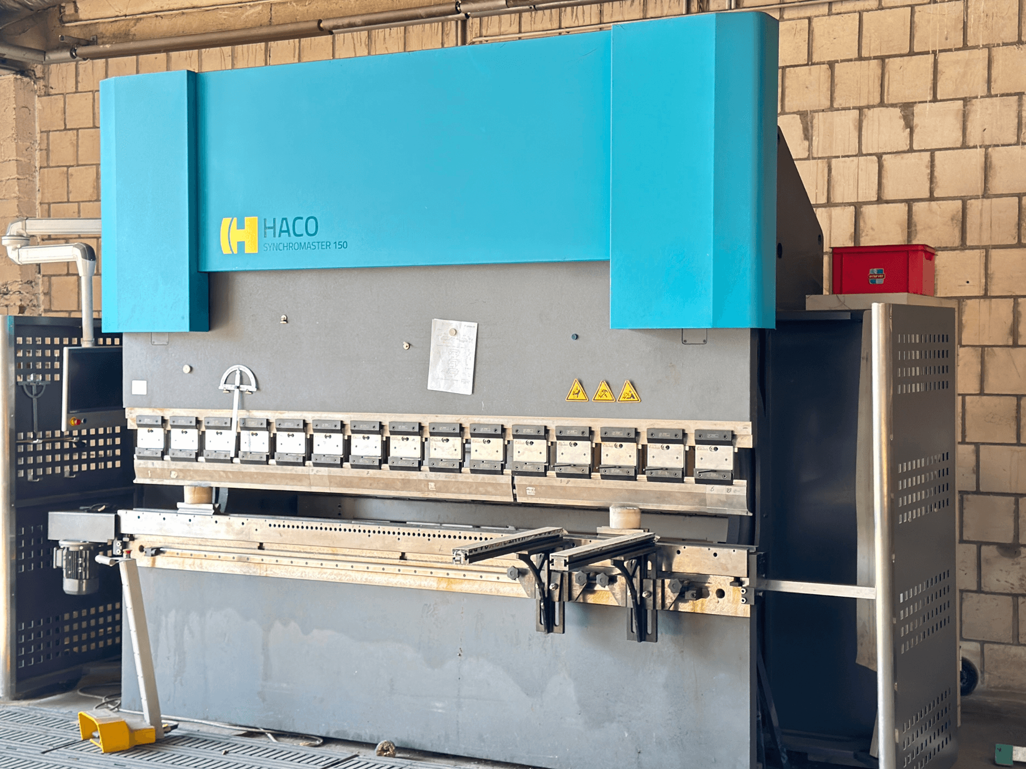 HACO SRM30150 présfék, elölnézet; a vezérlőpanel és a befogószerszámok, látható biztonsági figyelmeztető címkékkel.