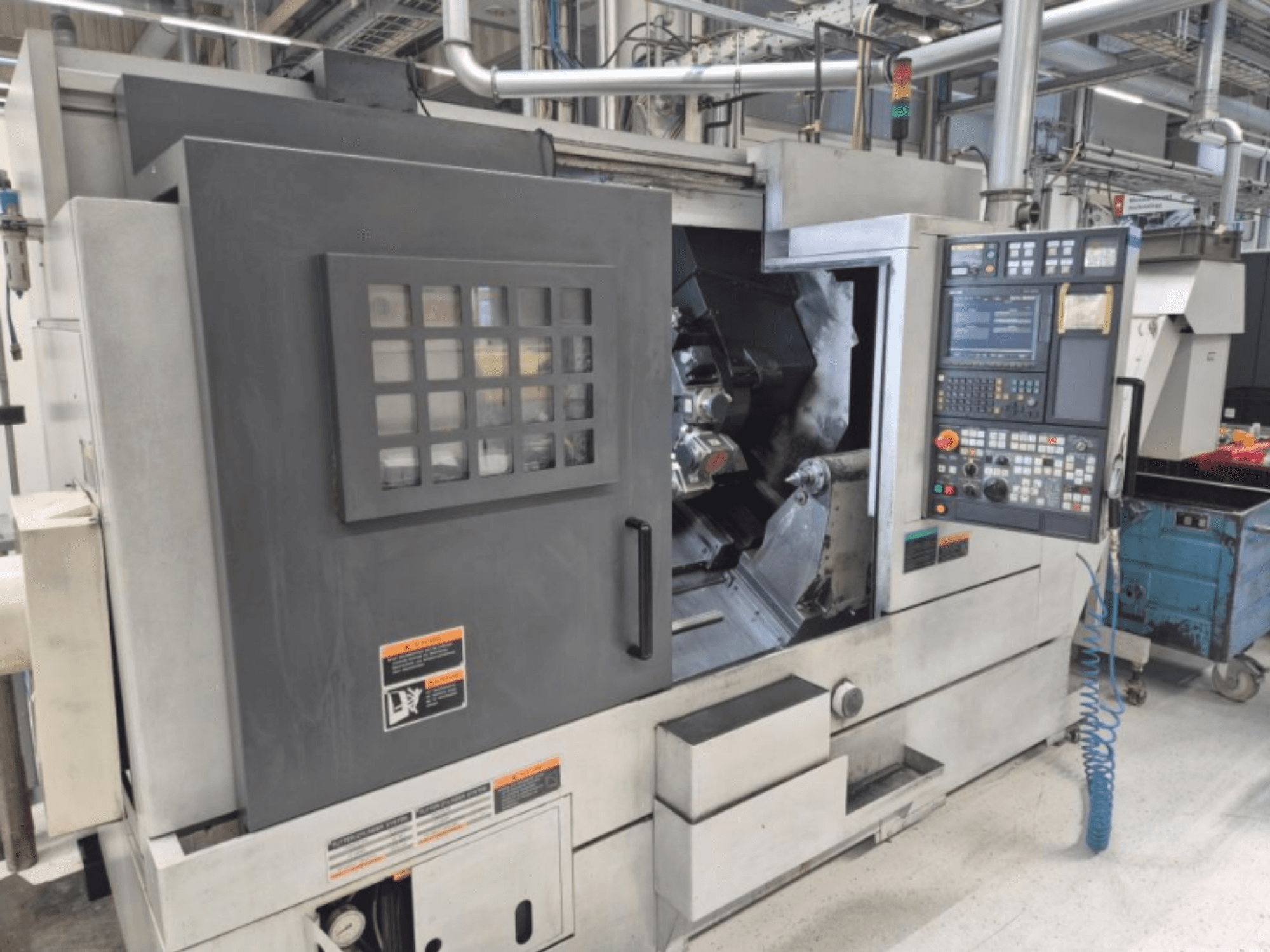 CNC esztergagép vezérlőpanellel, elölnézetből. Látható munkaterülettel és biztonsági ablakkal rendelkezik, márka ismeretlen.