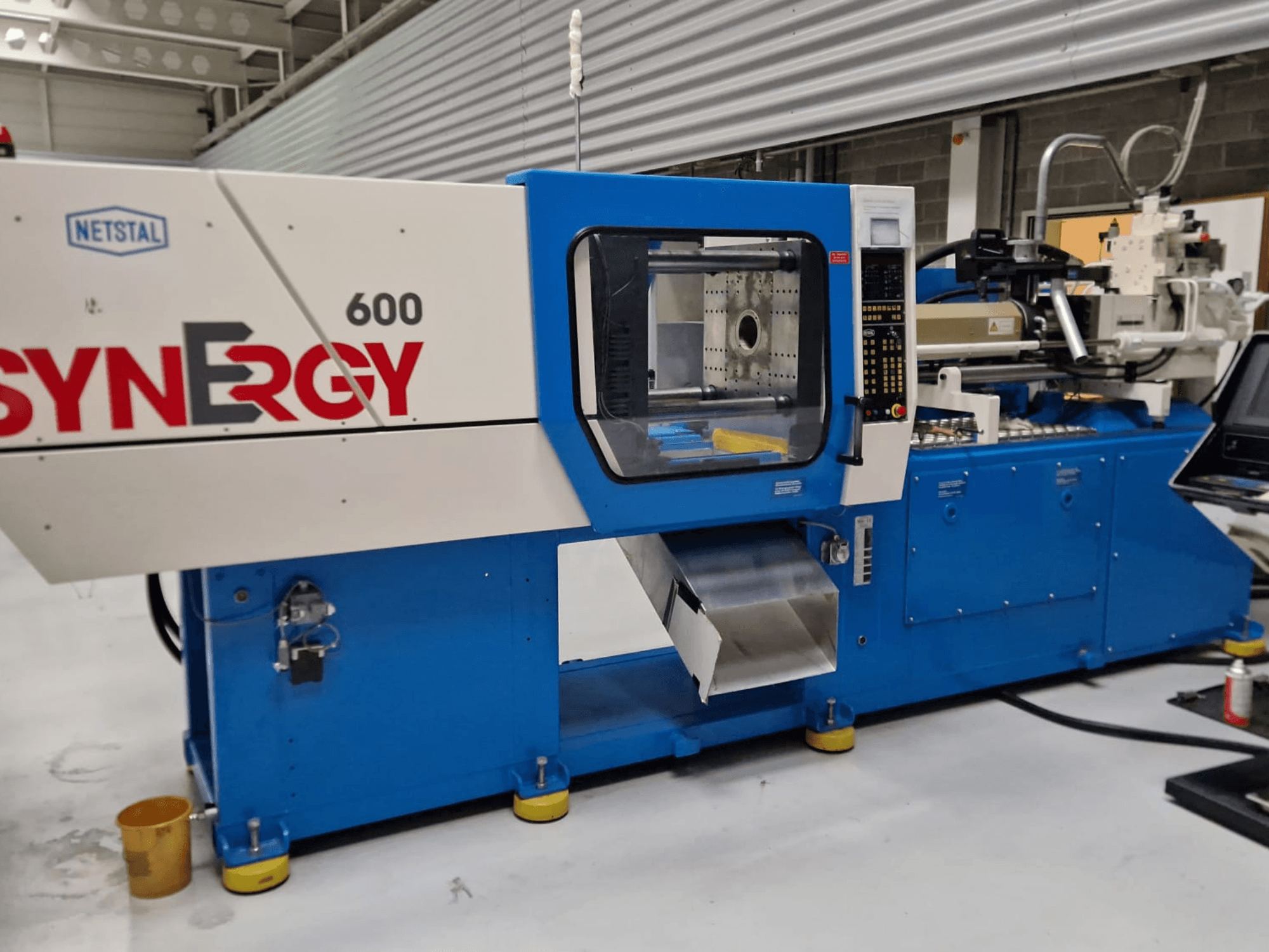 Netstal Synergy 600-230 hidraulikus fröccsöntőgép, oldalnézet a vezérlőpanel és a fröccsöntési területről.