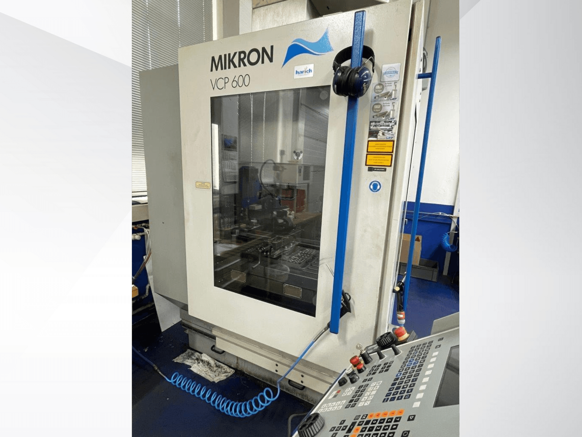 Mikron VCP 600 CNC-gép, előlnézet, gombokkal ellátott vezérlőpanel, üveg mögött látható megmunkálási terület.