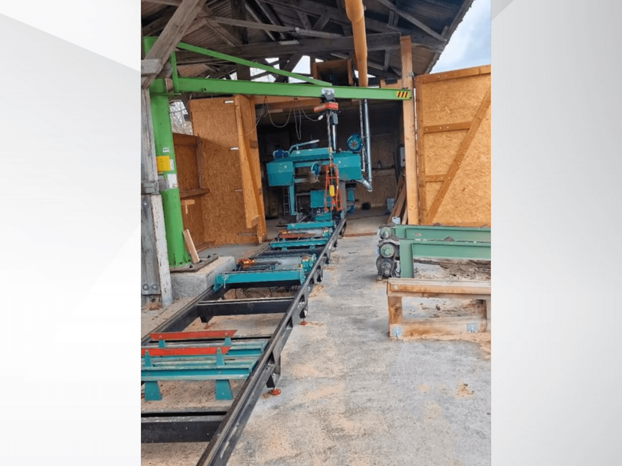 Vízszintes szalagfűrészgép műhelyben, szemből nézve. A berendezéshez tartozik egy pálya és további zöld tartozékok.