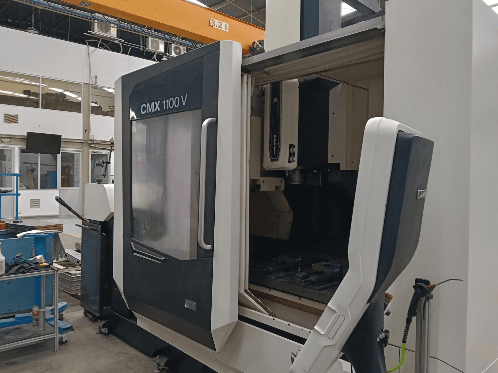 DMG MORI CMX 1100 V függőleges megmunkáló központ, elölnézet nyitott ajtóval és a belső szerszámelrendezéssel egy ipari térben.