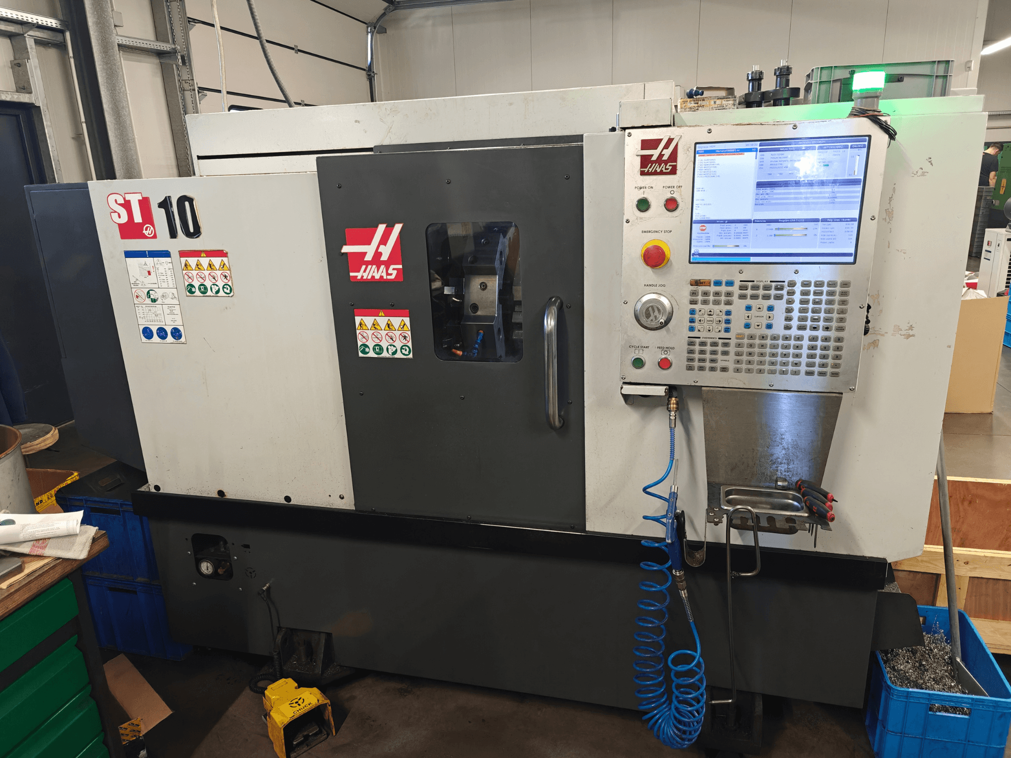 Haas ST-10 vízszintes eszterga, elölnézet, amelyen látható a vezérlőpanel, a biztonsági címkék és a gép felépítése.