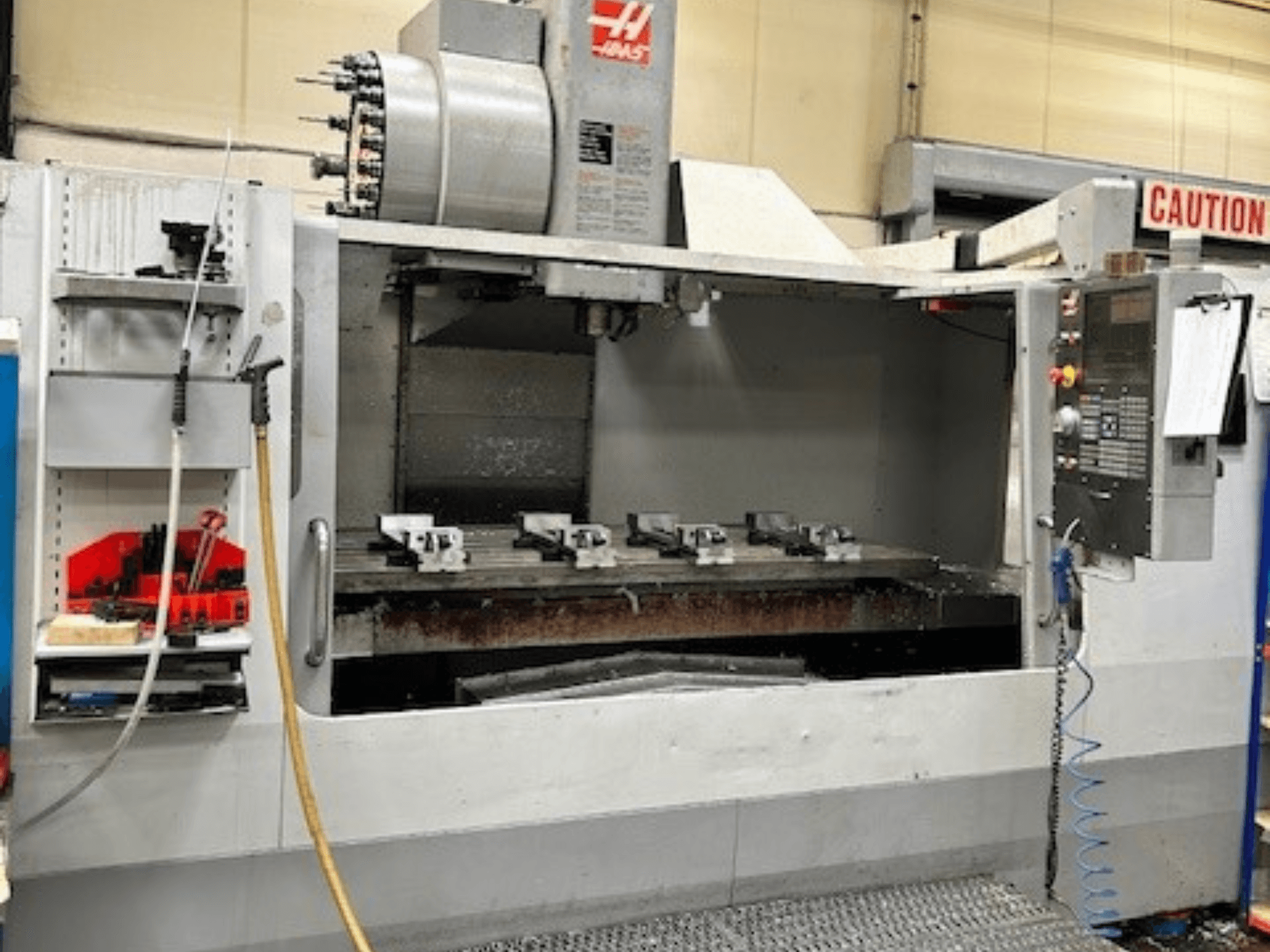 HAAS VF-9/40HE függőleges megmunkálóközpont, elölnézetben, szerszámtartóval és tartozékokkal az oldalán.