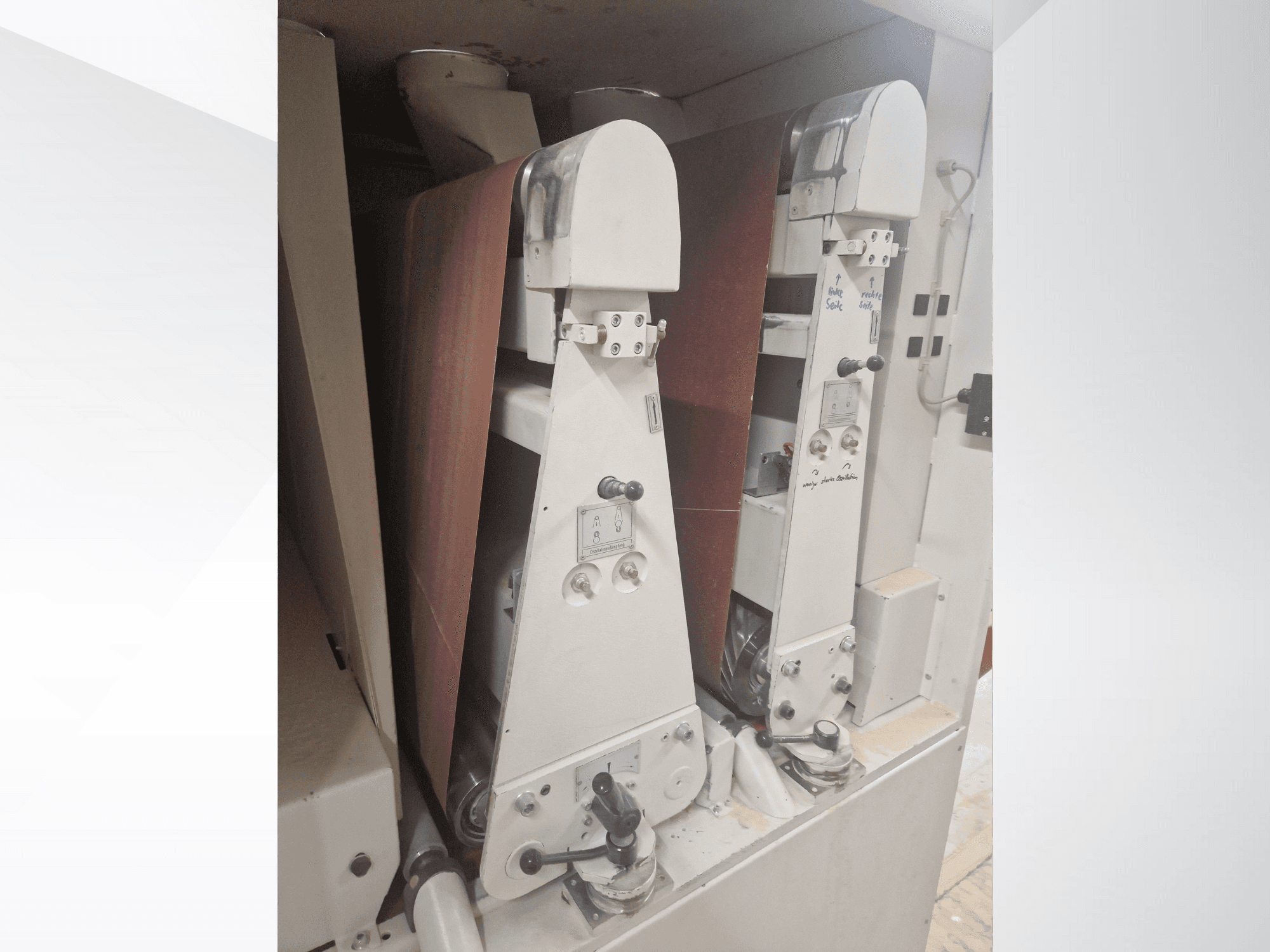 Két ipari csiszológép piros csiszolószalagokkal, elölnézetben, a kezelőszervek és a fém alkatrészek bemutatásával.