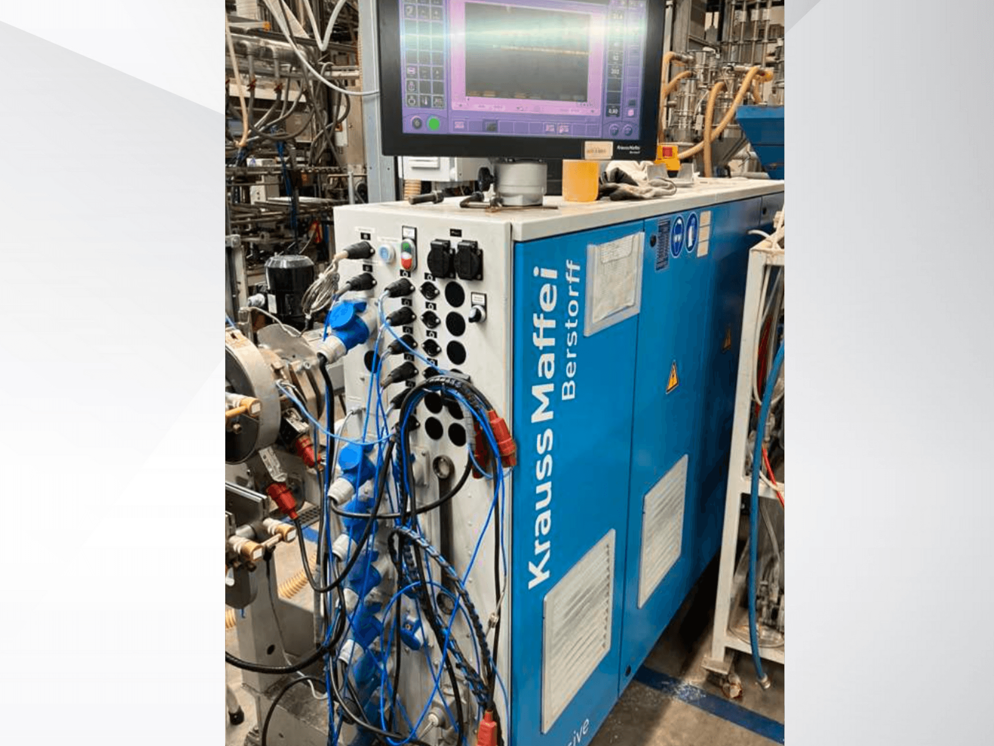 Krauss Maffei Berstorff ipari gép vezérlőpanellel és monitorral, különböző gombokkal és csatlakoztatott tömlőkkel, oldalnézet.
