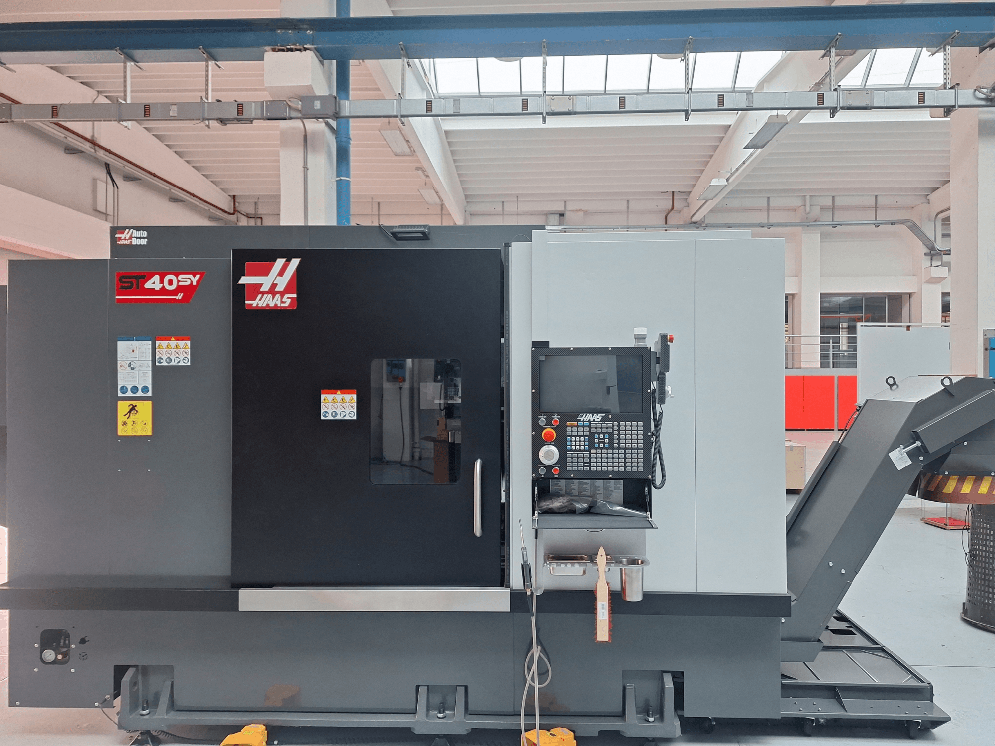 A Haas ST-40SY vízszintes eszterga oldalnézetben, a vezérlőpanellel és a biztonsági címkékkel együtt.
