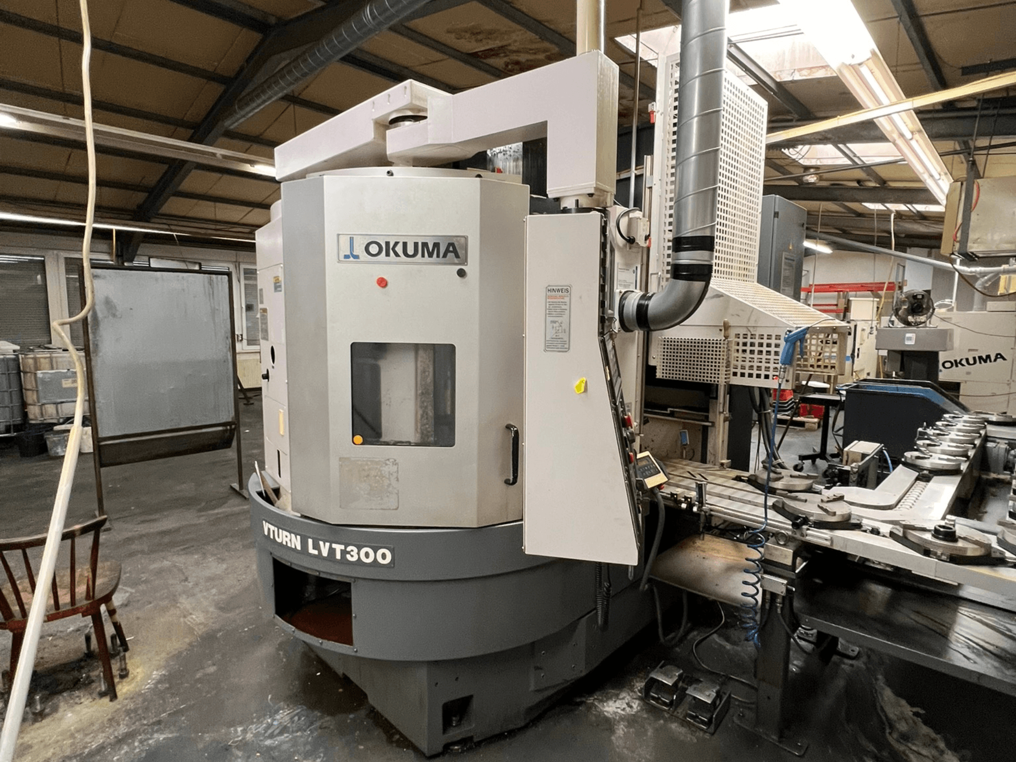 Okuma Vturn LVT300 CNC eszterga, oldalnézet ipari környezetben, a vezérlőpanel és a hűtőfolyadék-rendszer bemutatásával.