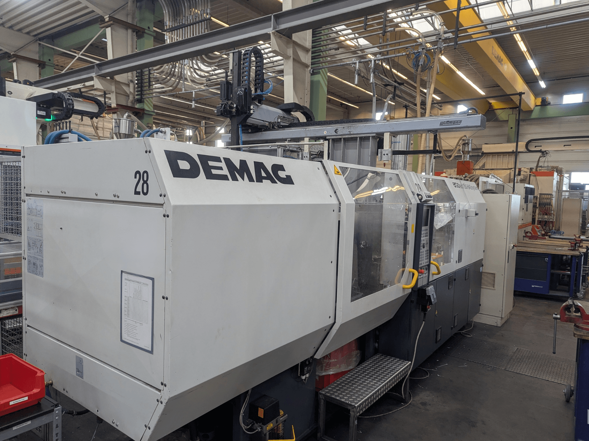 Egy DEMAG ERGOTECH 1500-840 hidraulikus fröccsöntőgép elülső nézete, a kezelőszervek és a biztonsági funkciók bemutatása.