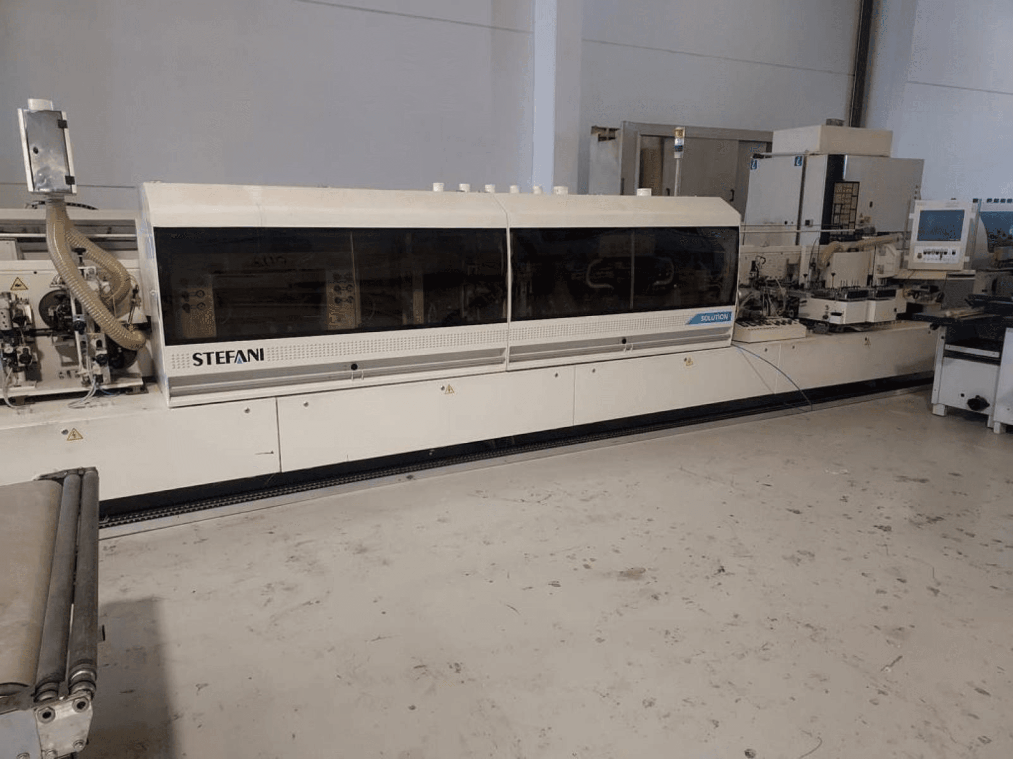 Stefani Solutions élszalagozó gép, elölnézetben, látható a porelszívó rendszer és a vezérlőpanel, műhelyben.