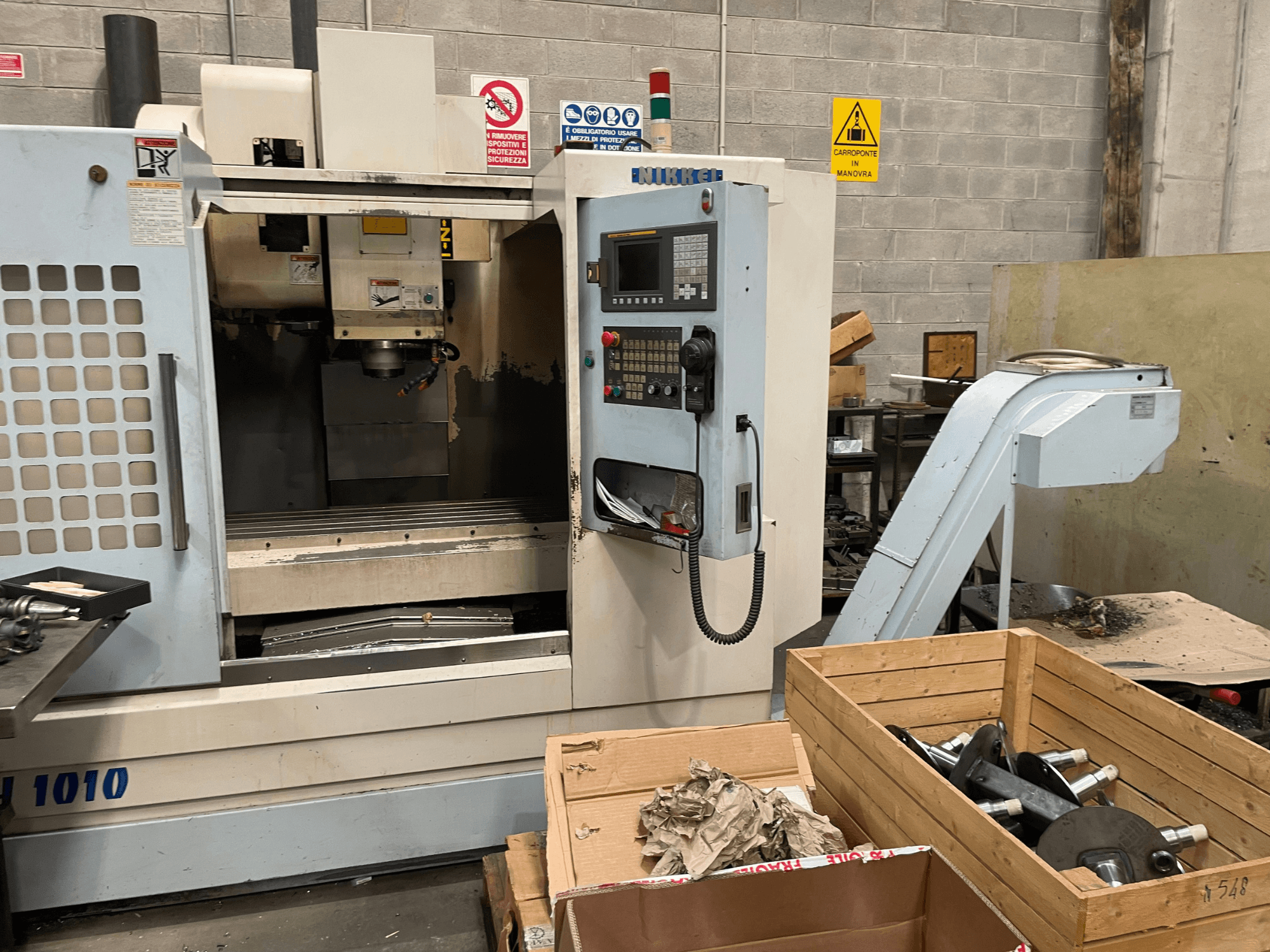 Az Other függőleges megmunkálóközpontja, VH-1010 modell, szemből nézve, a kezelőszervek láthatóak és a dobozok a közelben.